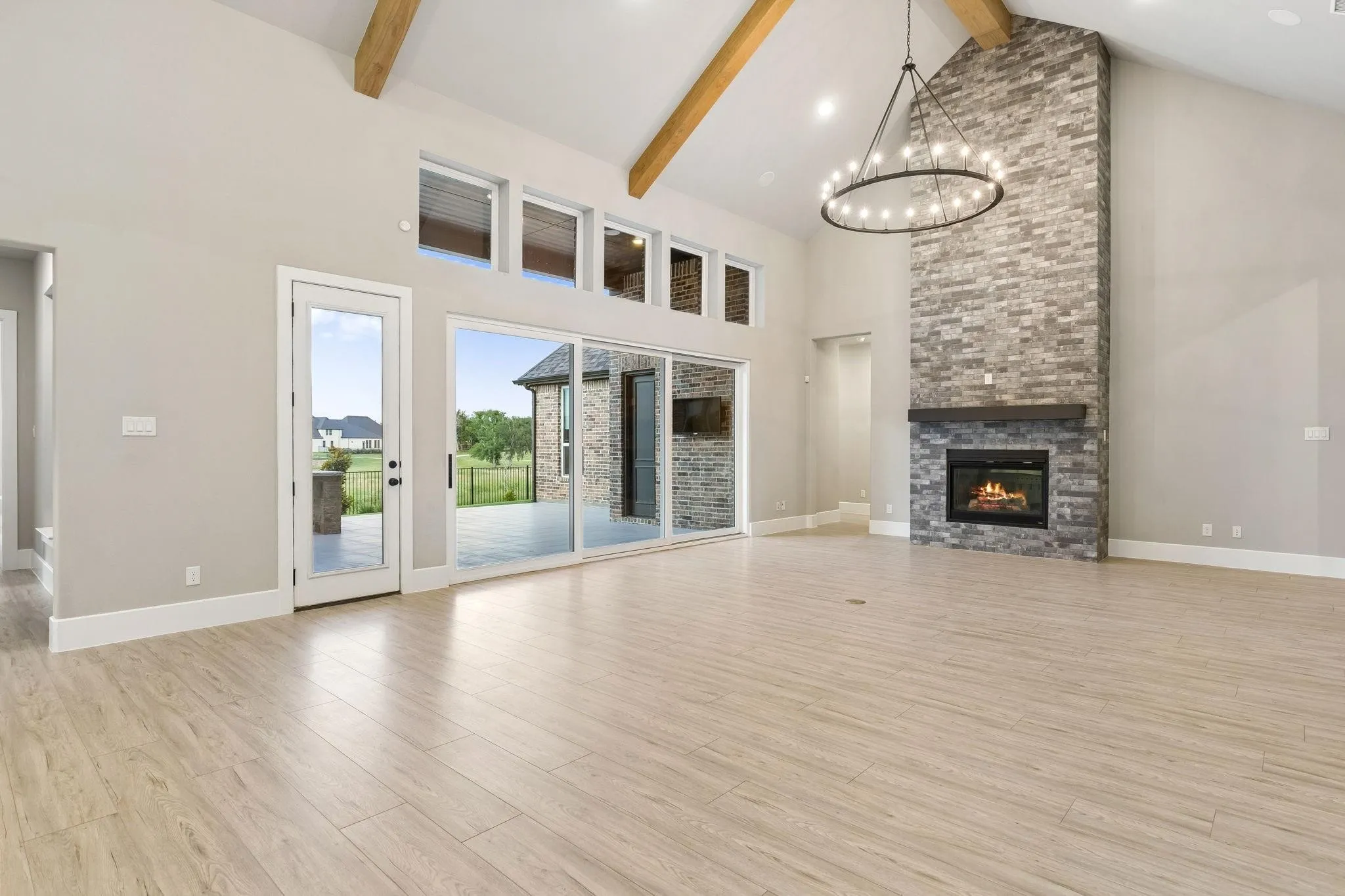 Vaulted ceiling with exposed wood beams, stone-clad fireplace with mantel, expansive sliding glass doors, transom windows, and wood-finish flooring