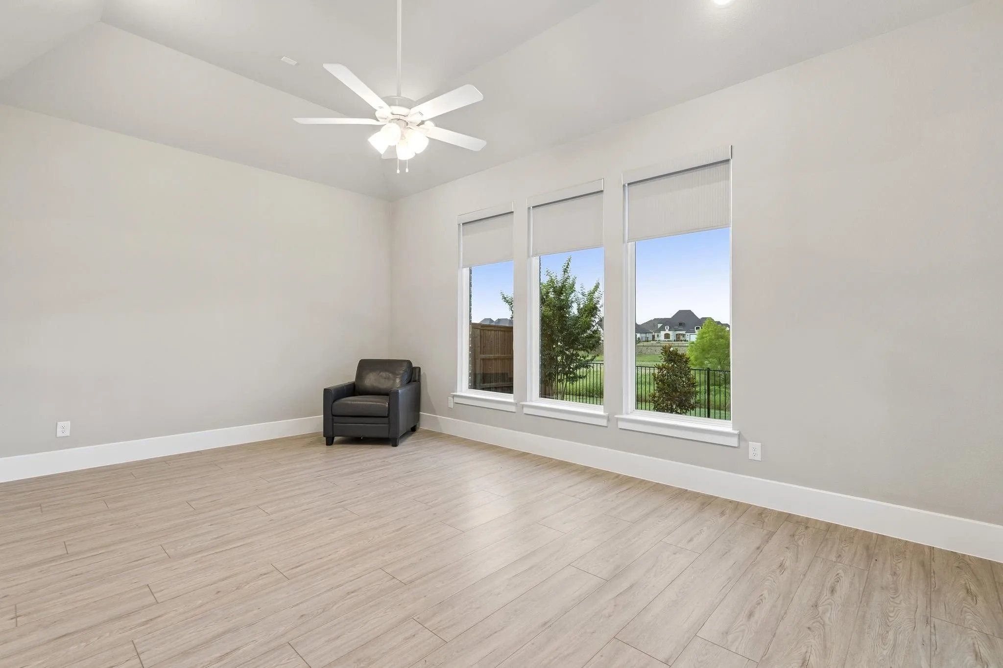 Tray ceiling with a ceiling fan, light-toned wood-finish flooring, and multiple large windows with roller shades