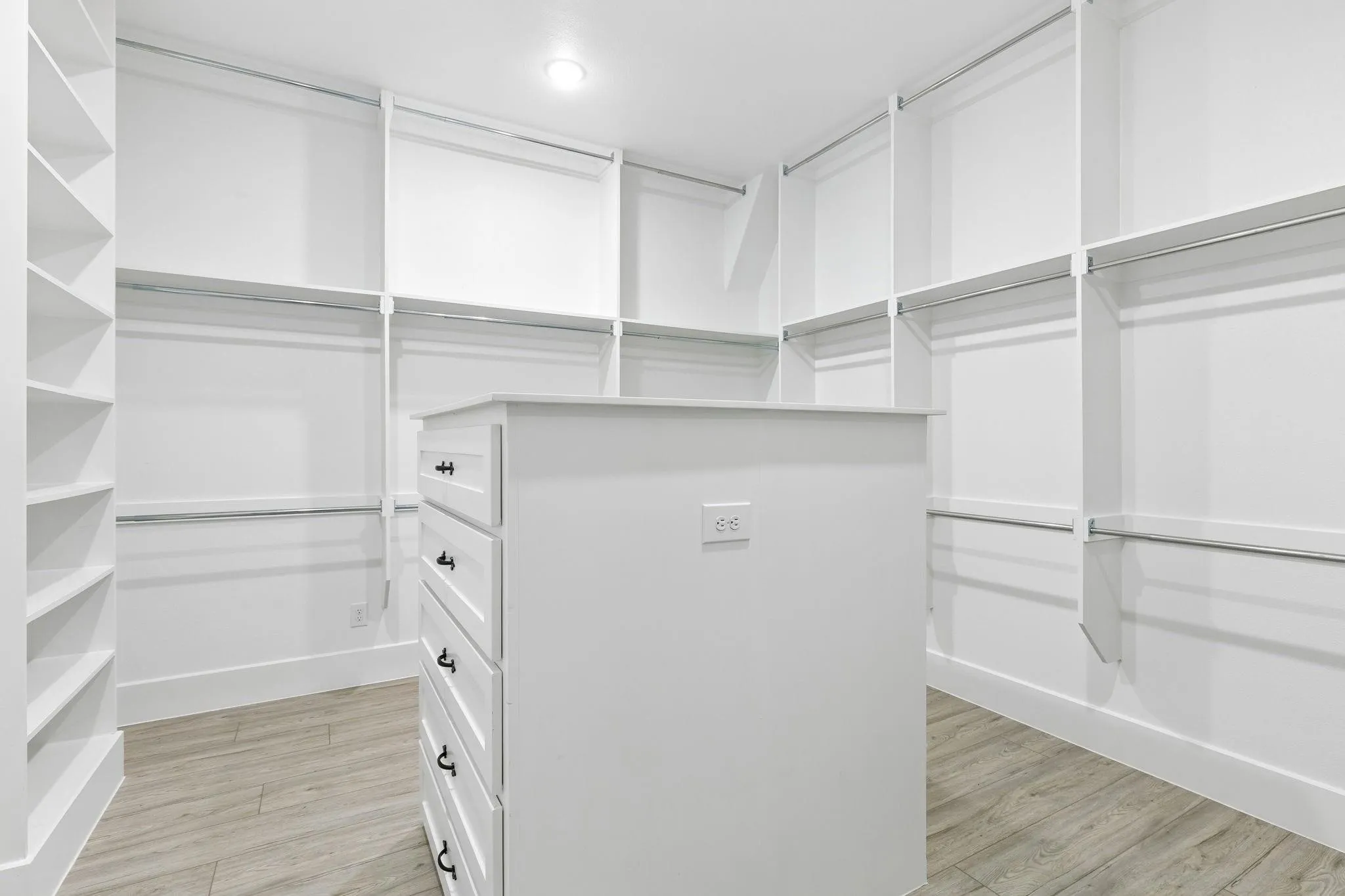 Luxurious walk-in closet featuring extensive built-in cabinetry with multiple shelving sections, a central island with five drawers, wood-finish flooring, and recessed lighting throughout for optimal visibility and organization