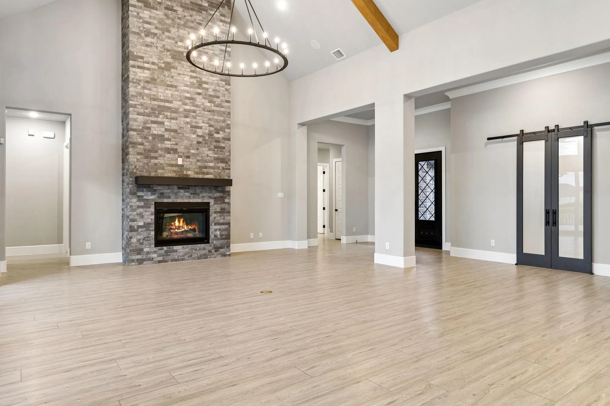 Spacious great room featuring vaulted ceilings, a stone fireplace with a wood mantle, wood-finish flooring, and a large chandelier