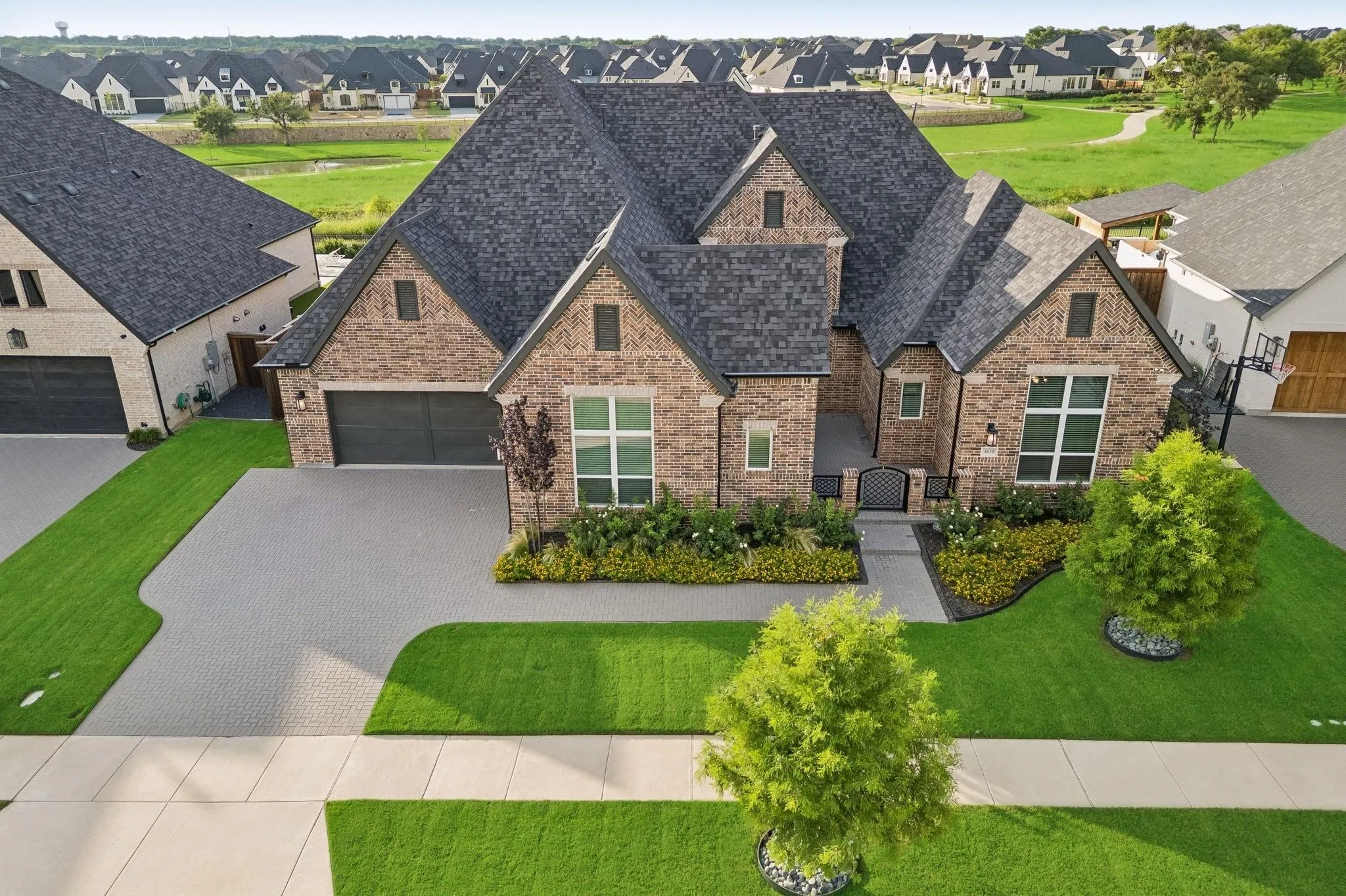Brick exterior with multiple gables, a dark shingle roof, paver driveway, and a manicured lawn
