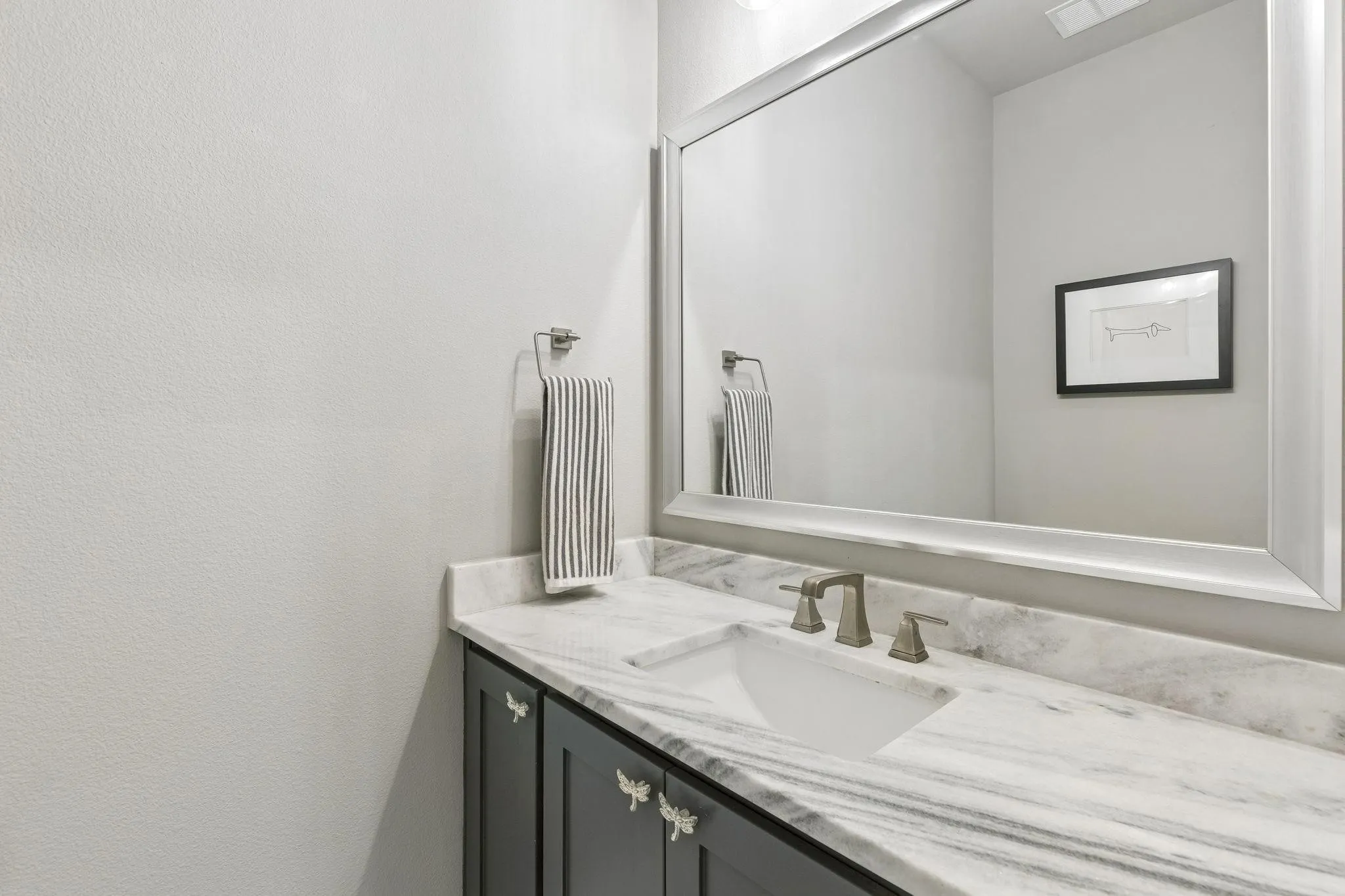 Vanity with an undermount sink, a stone-finish countertop, dark cabinetry, and a framed wall mirror