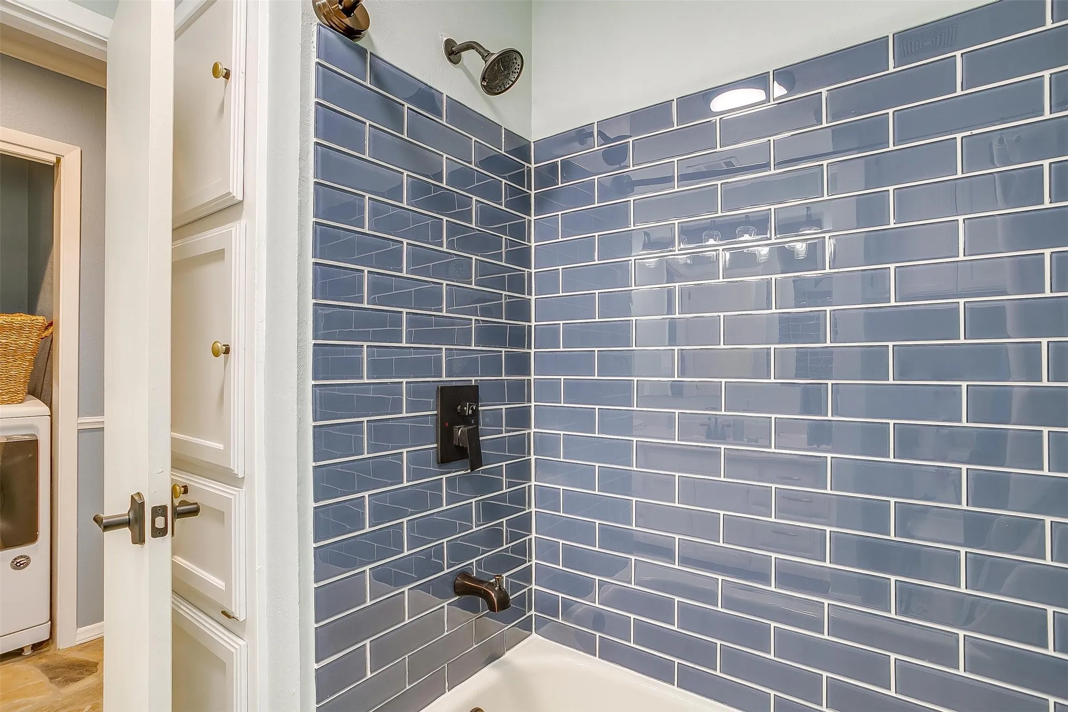Bathtub with blue subway tile surround and dark bronze fixtures