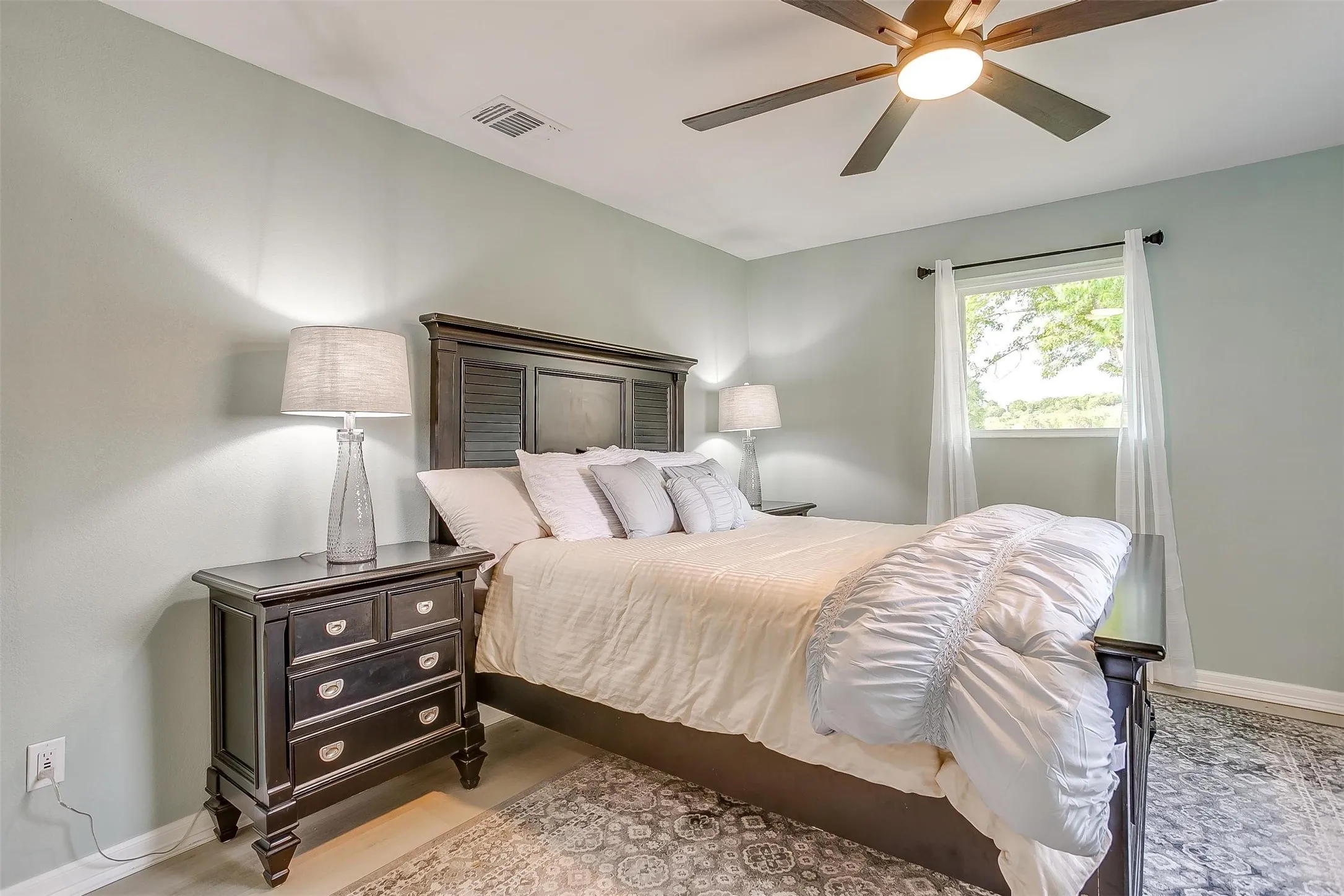 Recessed lighting, ceiling fan with integrated lighting, window with white curtains, wood-finish flooring