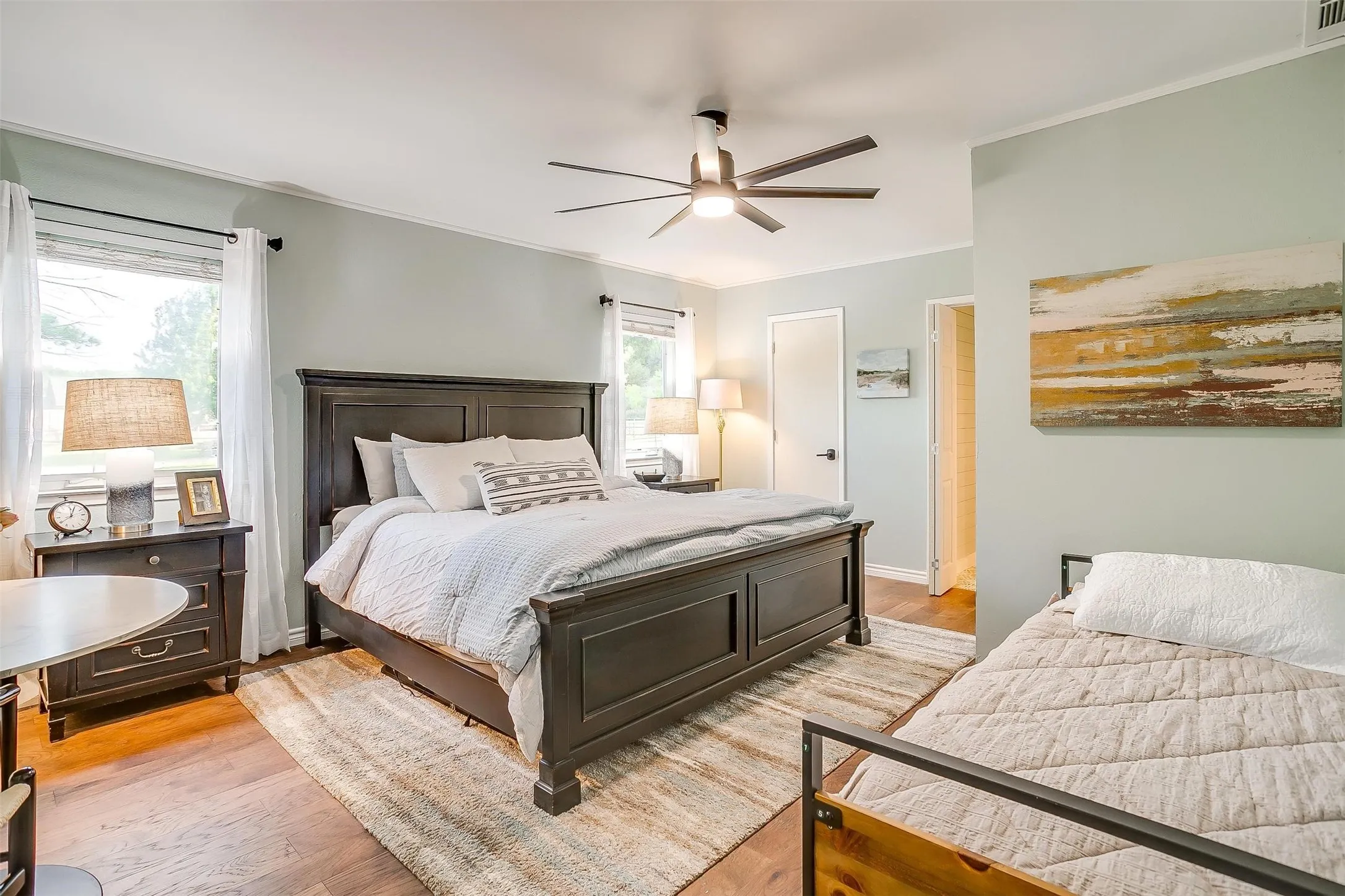 Wood-finish flooring, ceiling fan with integrated lighting, multiple windows, and light-colored walls