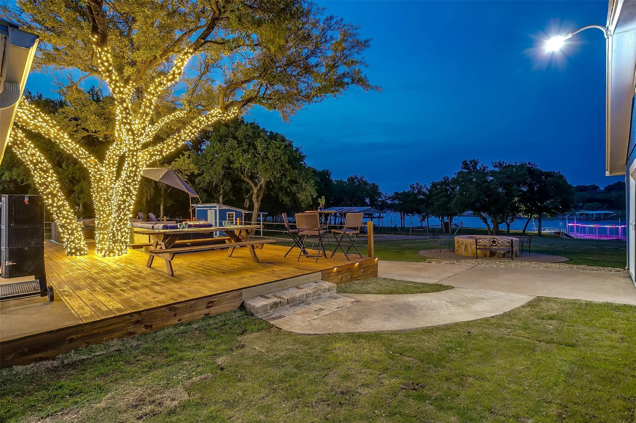 Expansive outdoor deck with wood-finish surface, integrated tree lighting, and a fire pit area