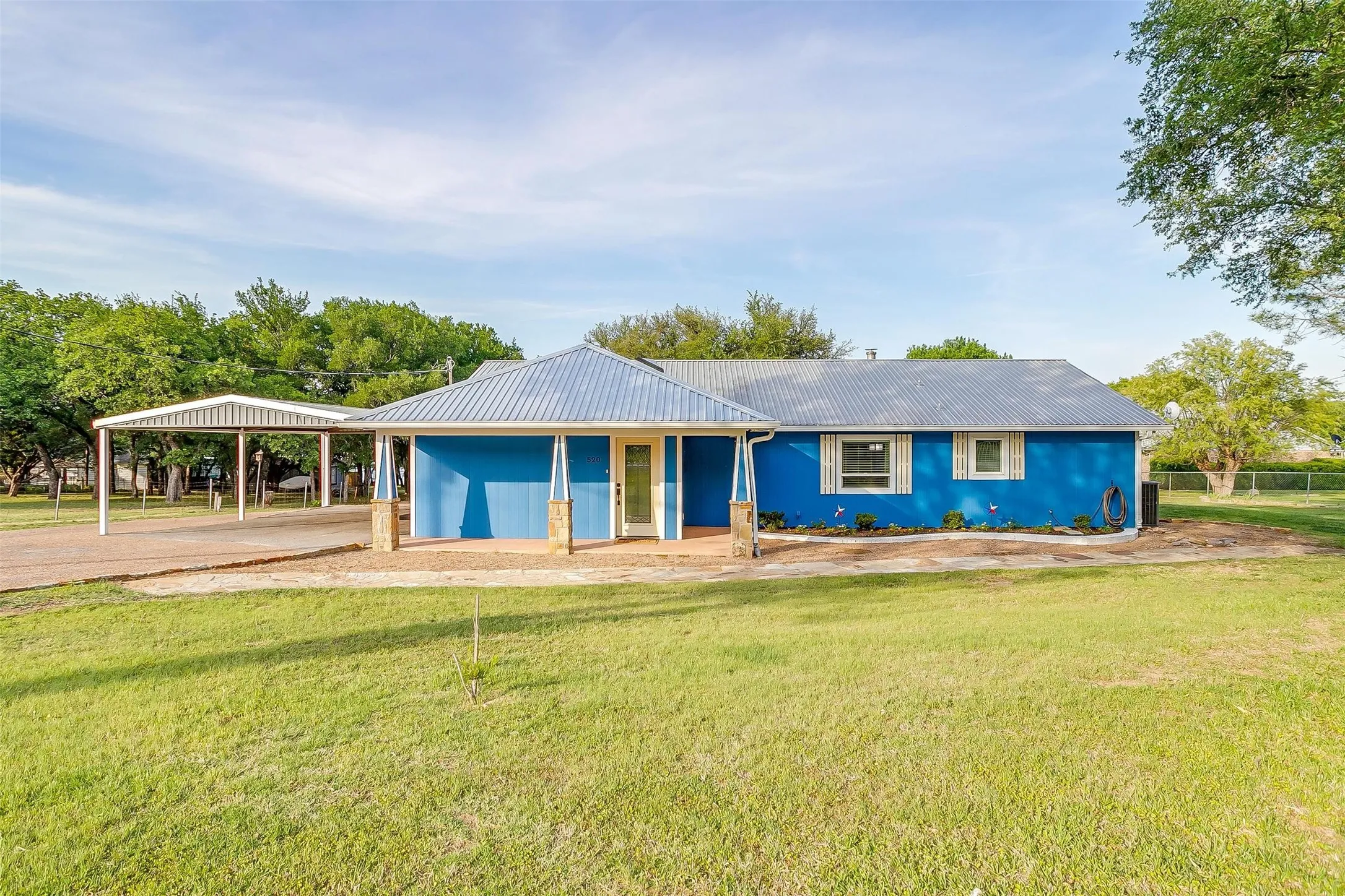 Single-story exterior with a metal roof, carport, vibrant blue siding, and a covered porch with stone-clad columns