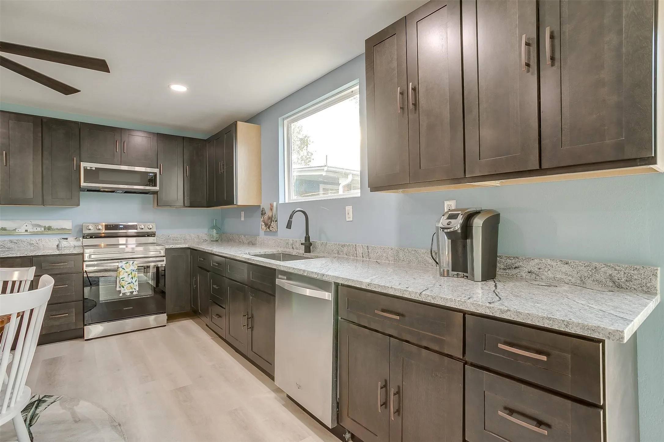 Expansive kitchen featuring dark wood cabinetry, light-toned countertops, stainless steel appliances, and wood-finish flooring