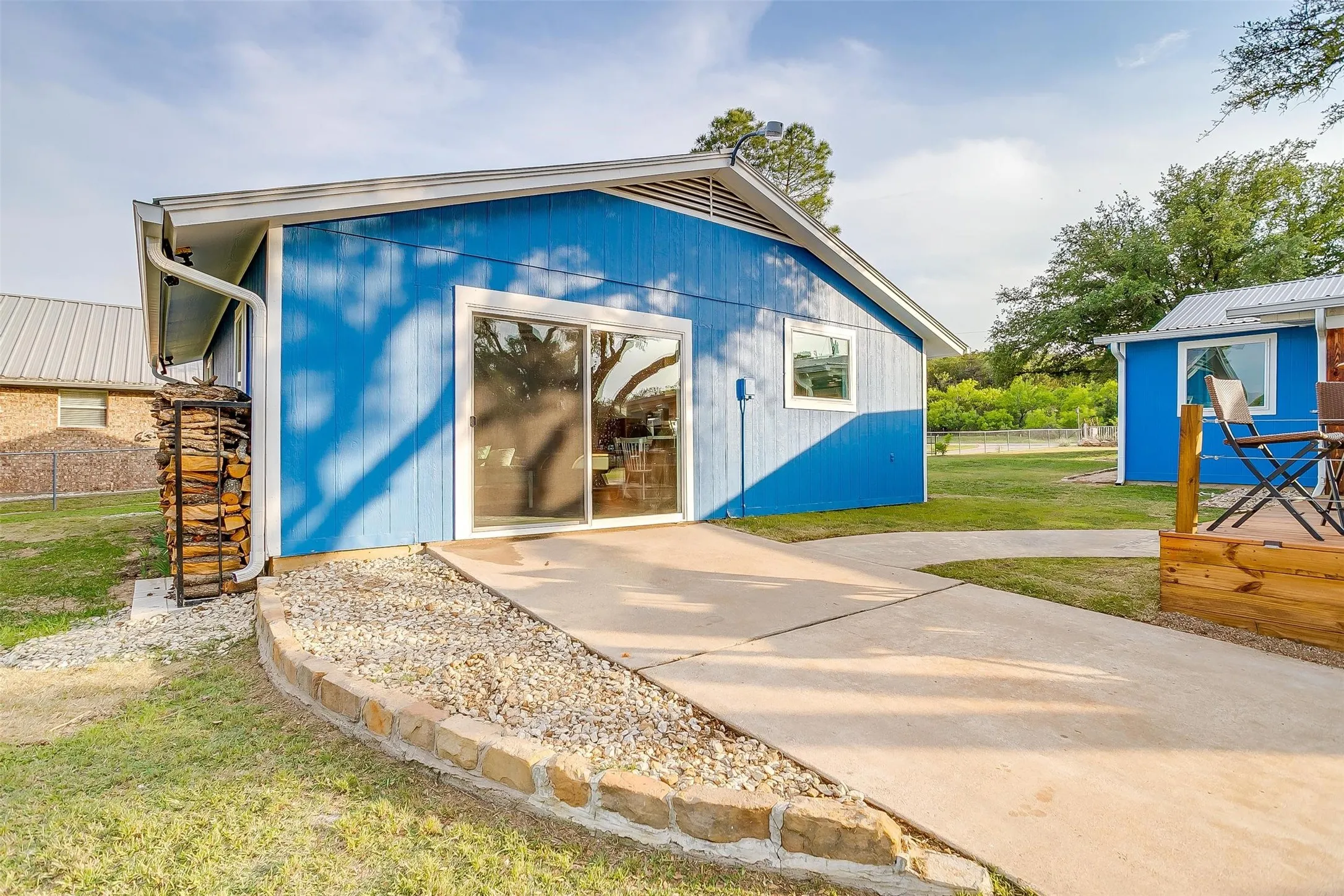 Blue siding exterior with white trim, concrete patio, sliding glass door, and stone-lined planter with gravel