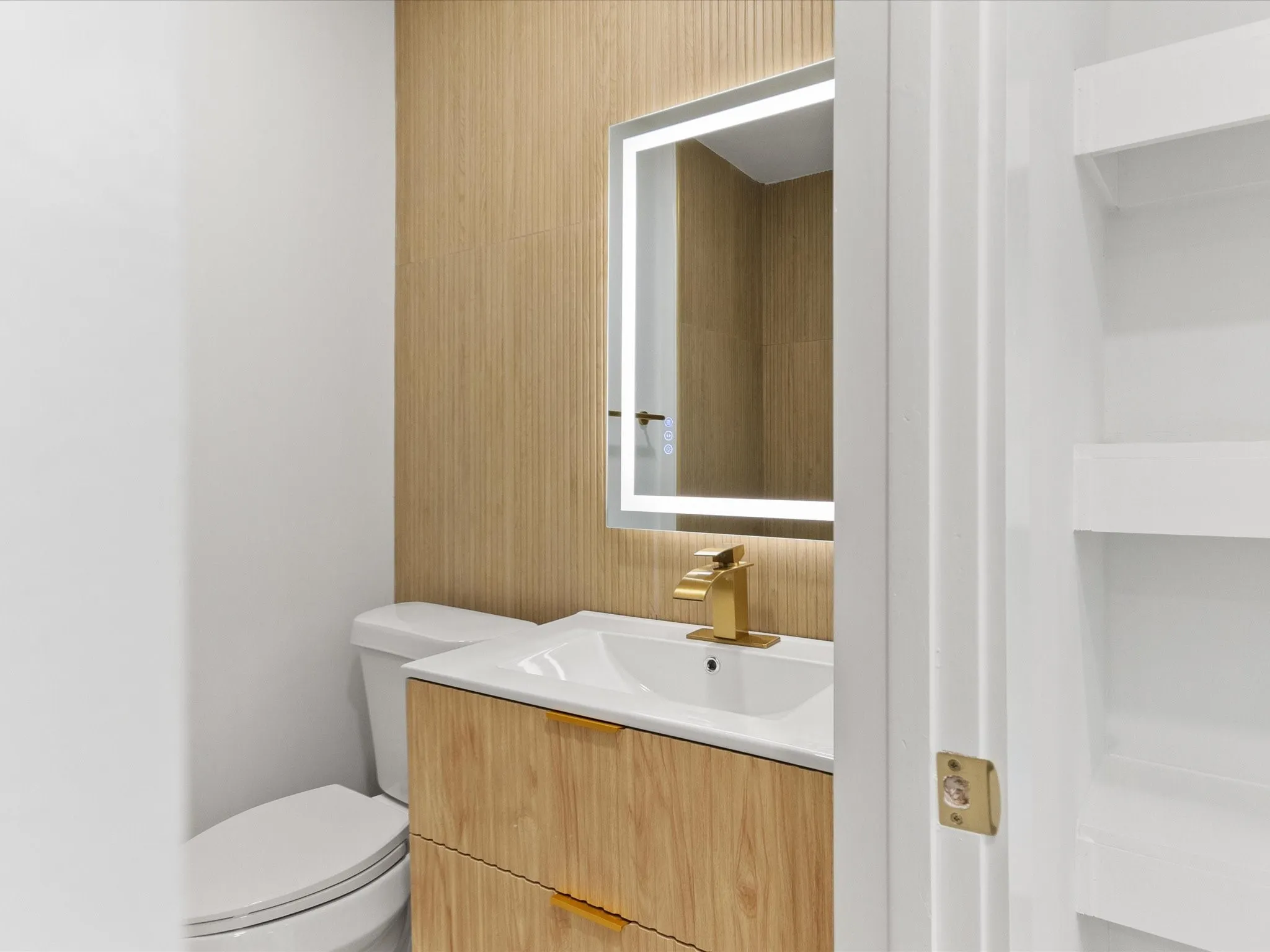 Integrated vanity with a gold-finish faucet, illuminated mirror, and wood-finish wall paneling