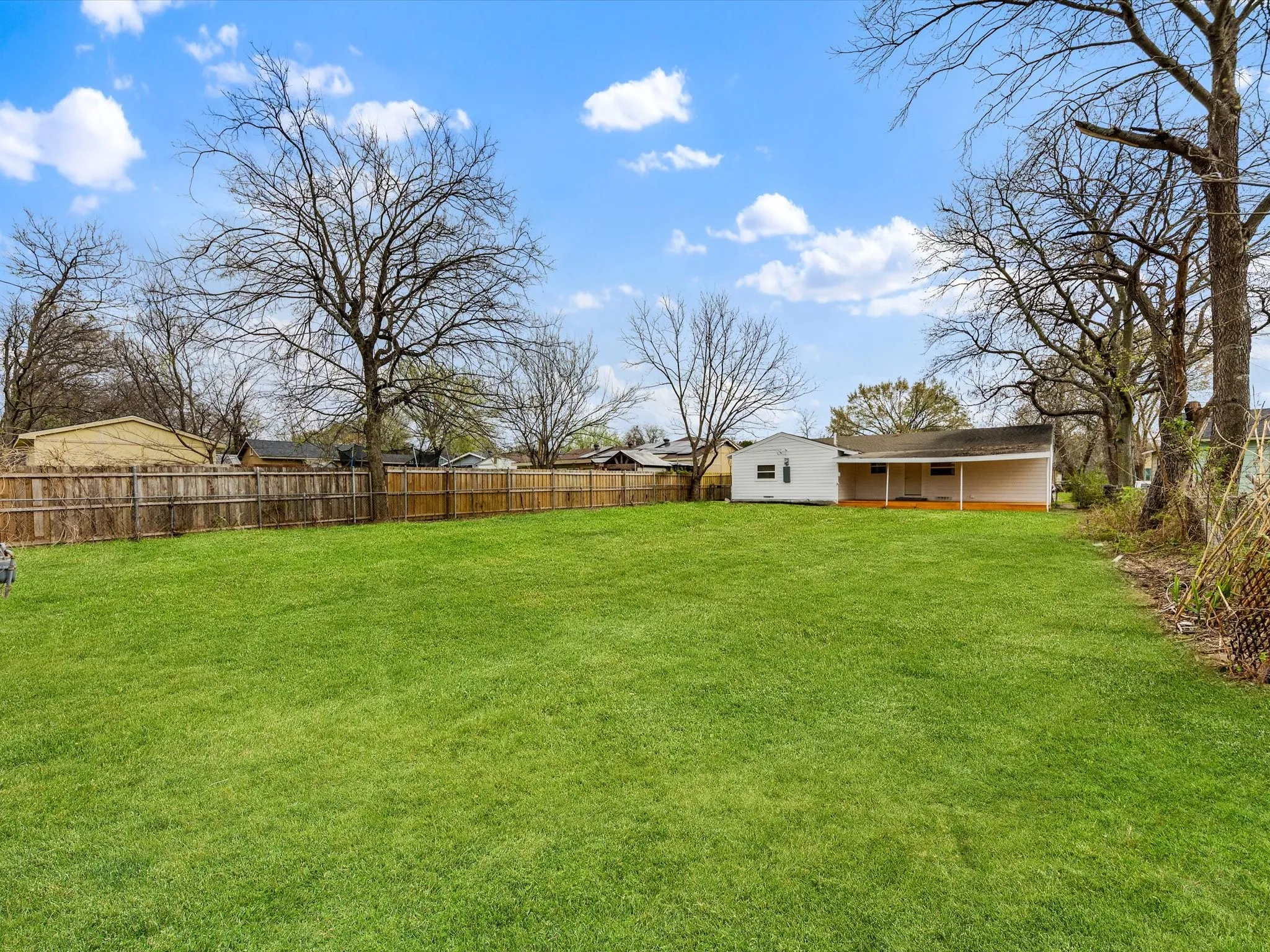 Expansive grassy yard with wood fencing and mature trees