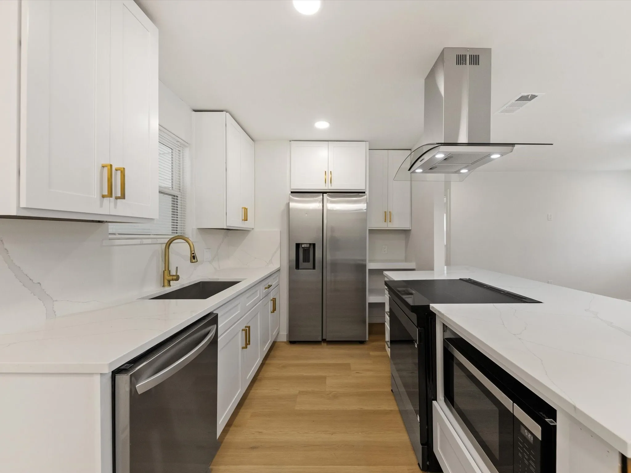 White shaker cabinetry with gold-tone hardware, stainless steel appliances, white countertops, and wood-finish flooring