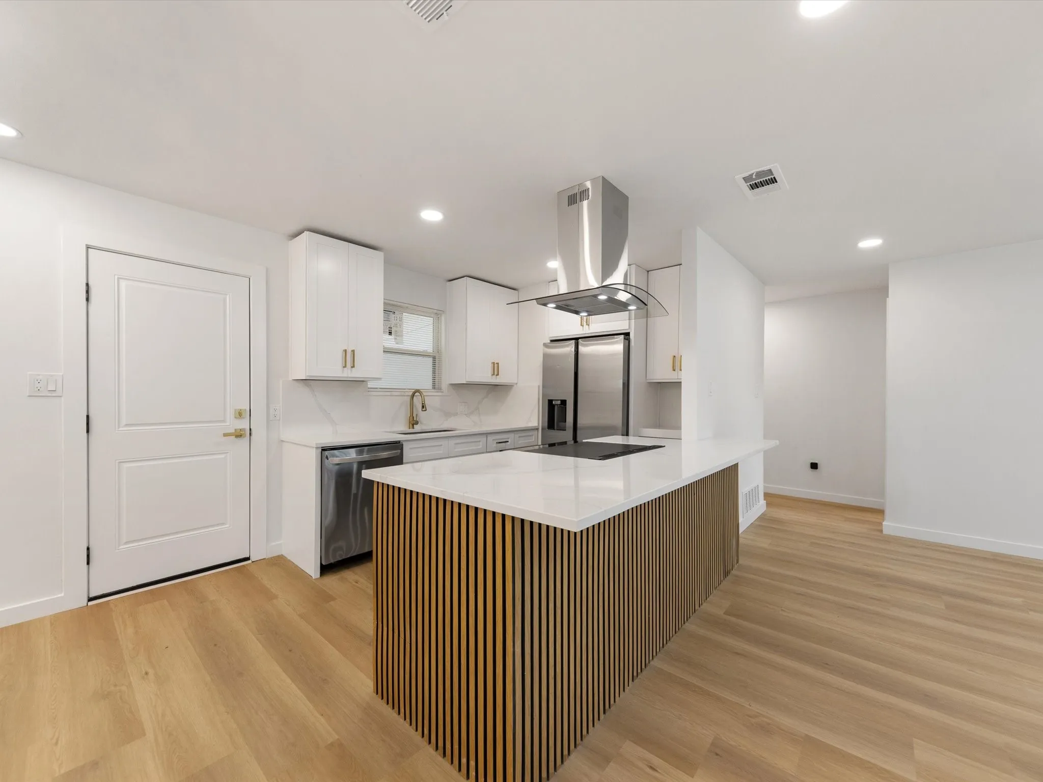 Kitchen featuring a wood-slatted island with a white countertop, stainless steel appliances, and white cabinetry with gold-finish hardware