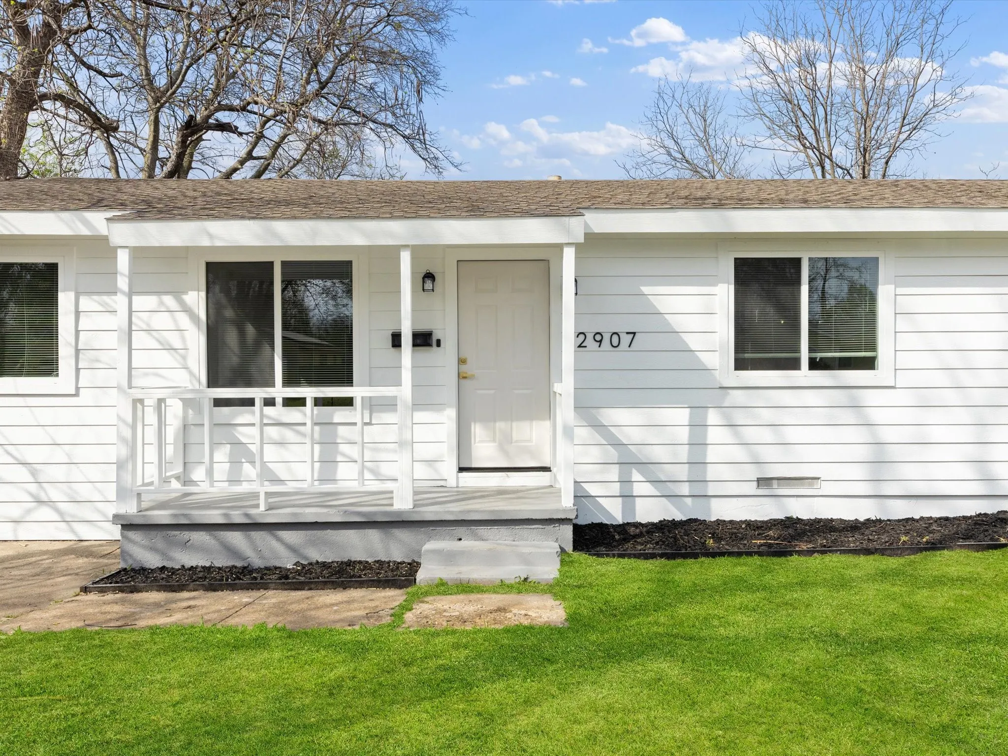 White siding exterior featuring a covered porch with white railings, a front entry door, and multiple windows