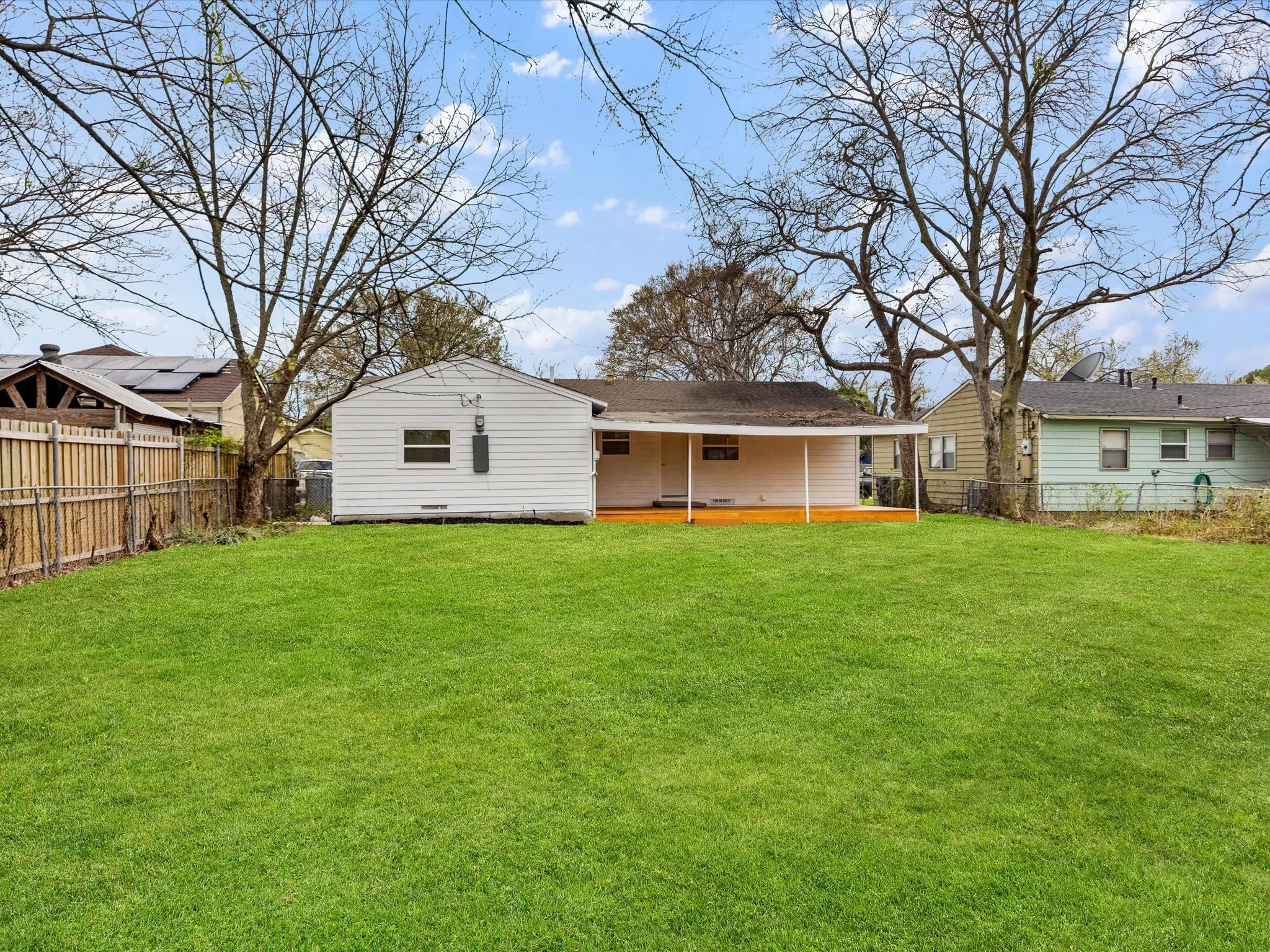 Expansive lawn with a wooden privacy fence, mature trees, and a covered patio