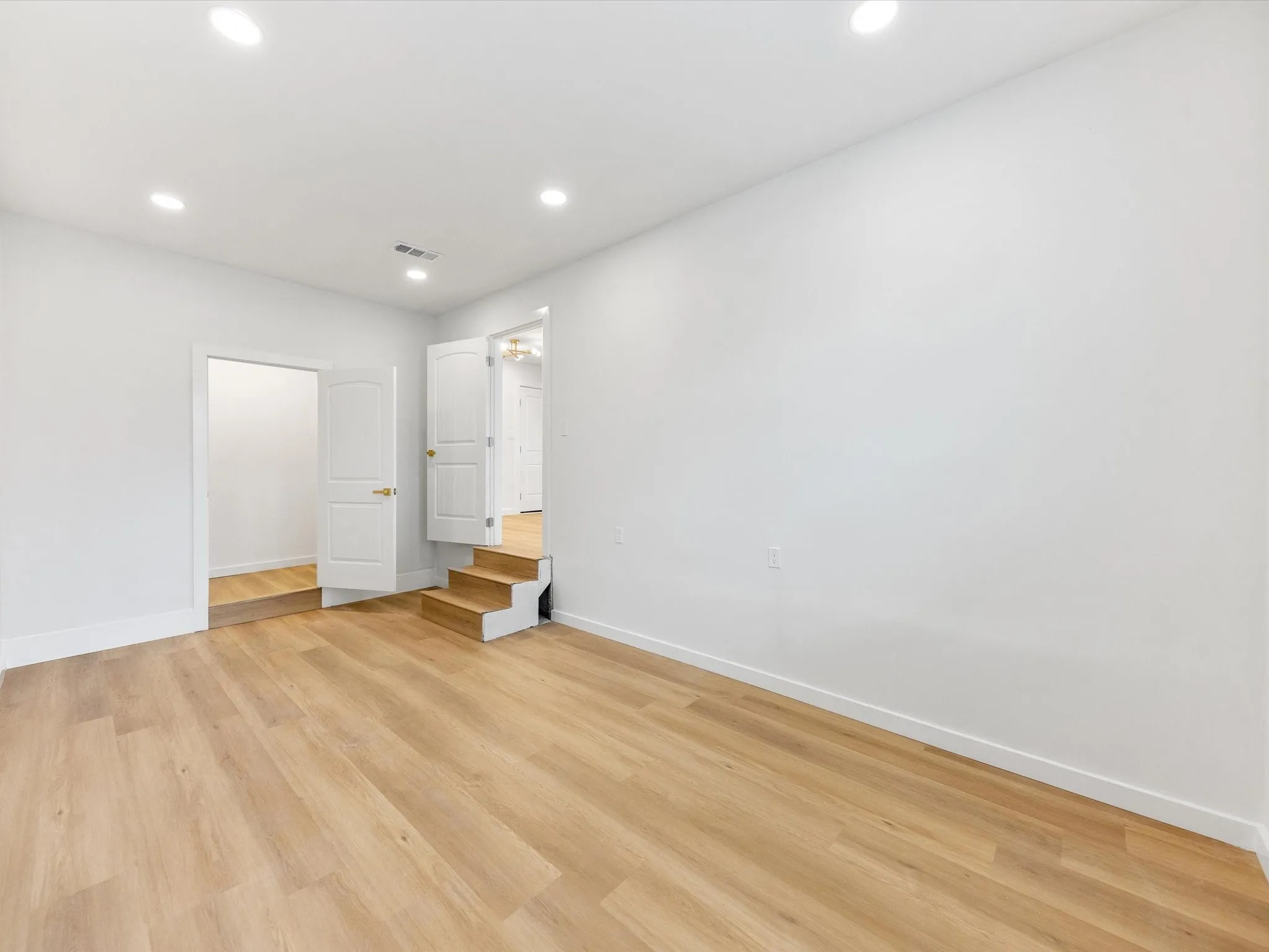Recessed lighting, wood-finish flooring, white walls, white trim, and white doors with brass hardware