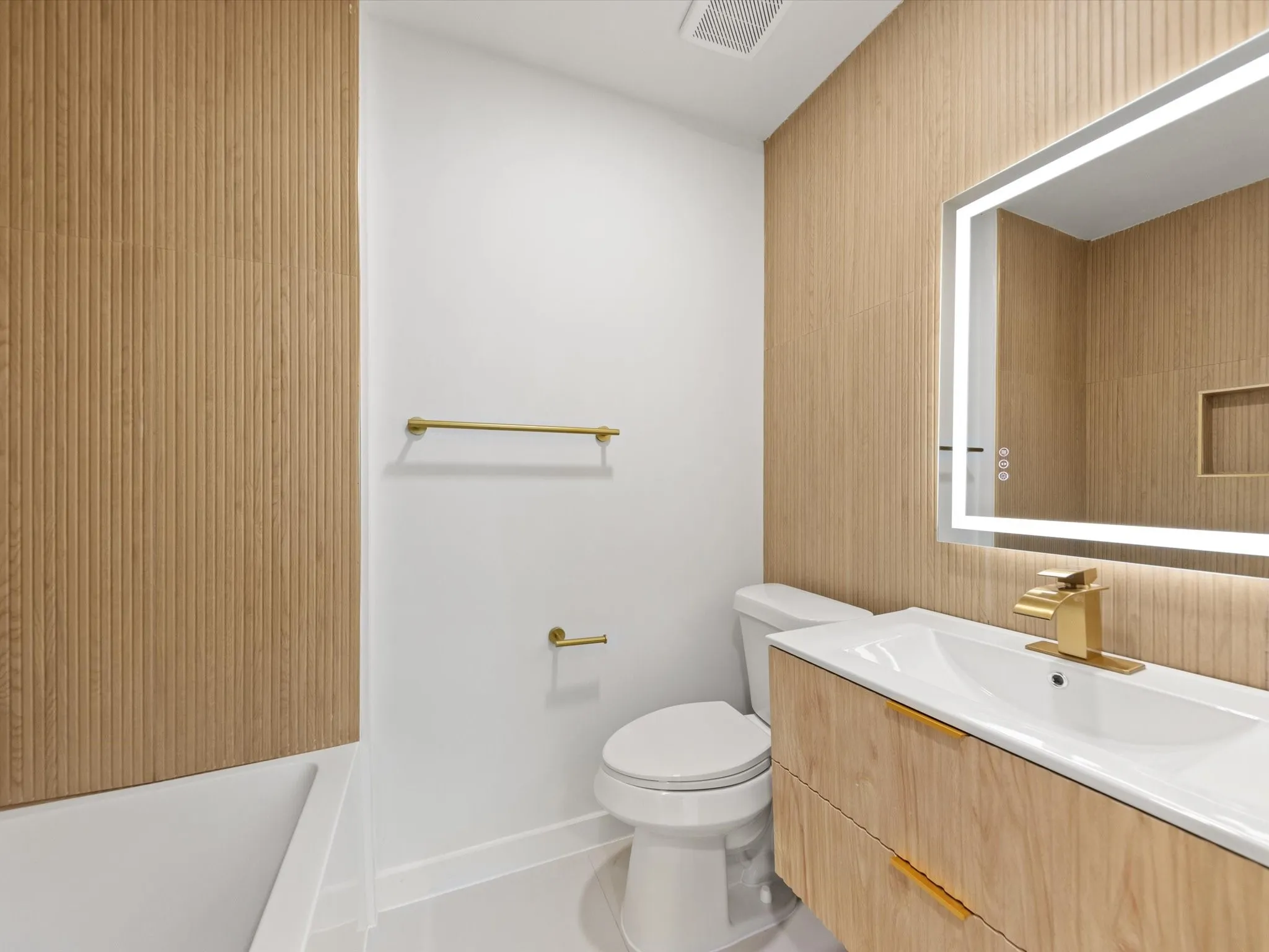 Wood-finish fluted paneling, integrated LED vanity mirror, wall-mounted gold-tone hardware, and a built-in shower niche