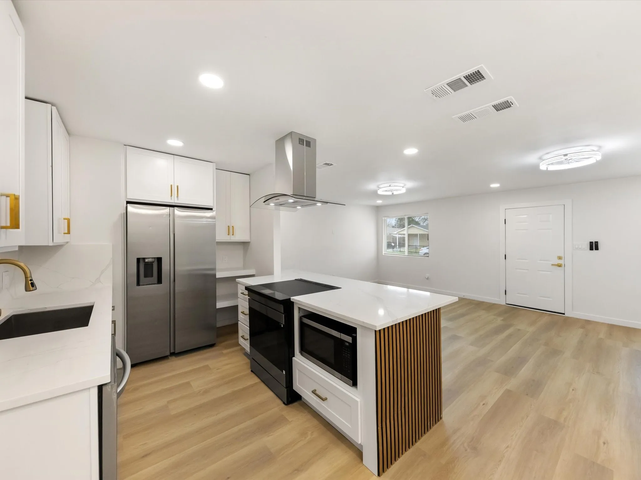 Contemporary kitchen featuring white cabinetry, stainless steel appliances, a center island with integrated microwave, wood-finish flooring, and recessed lighting