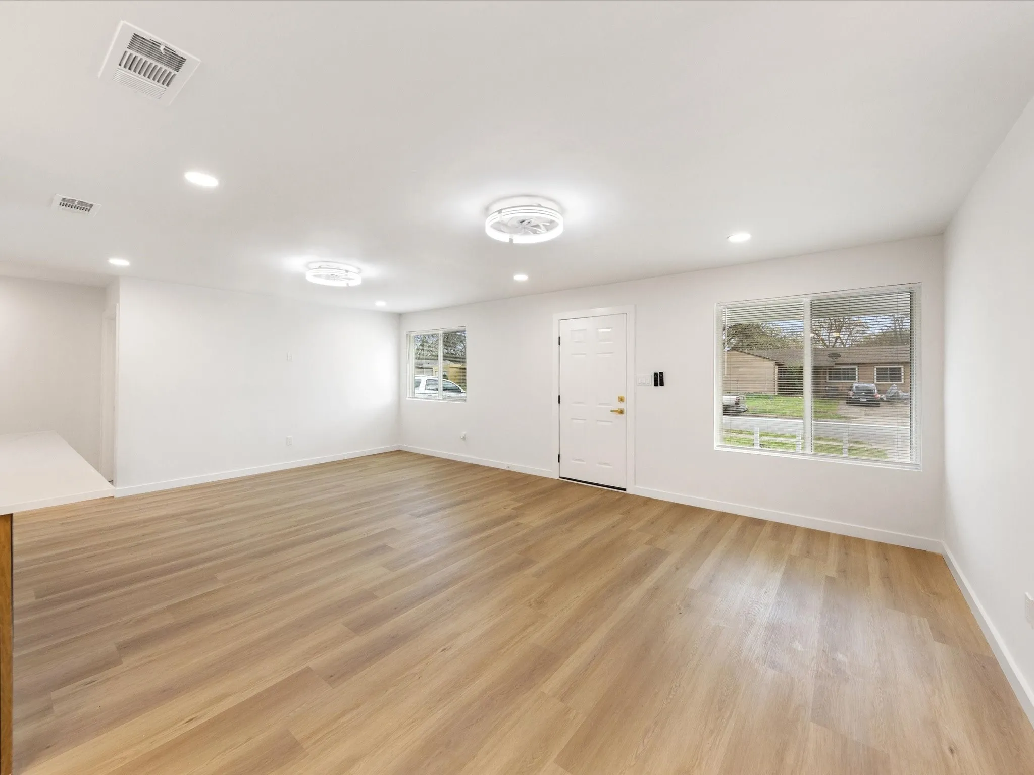 Recessed lighting throughout, wood-finish flooring, white walls, and a solid entry door with a multi-pane window