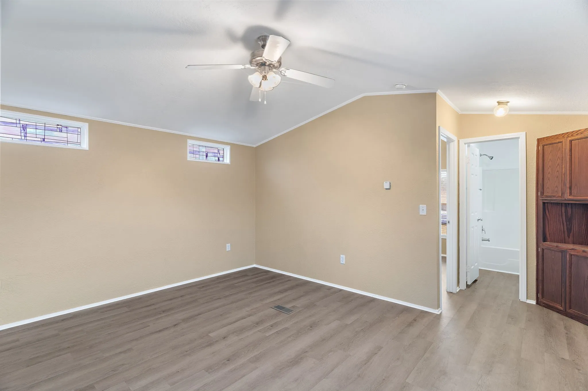 Empty room with ceiling fan, vaulted ceiling, crown molding, and light hardwood / wood-style floors