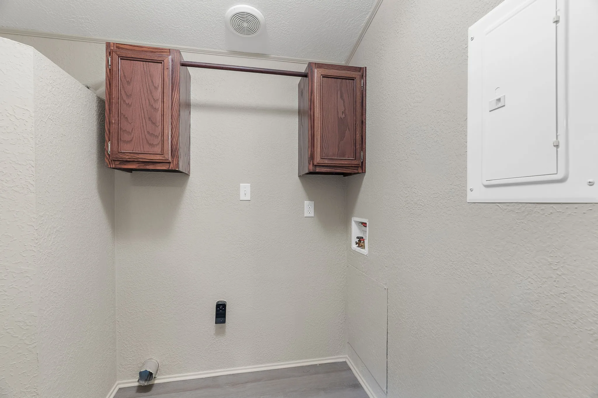 Laundry room with electric panel, a textured ceiling, hookup for a washing machine, cabinets, and hardwood / wood-style flooring