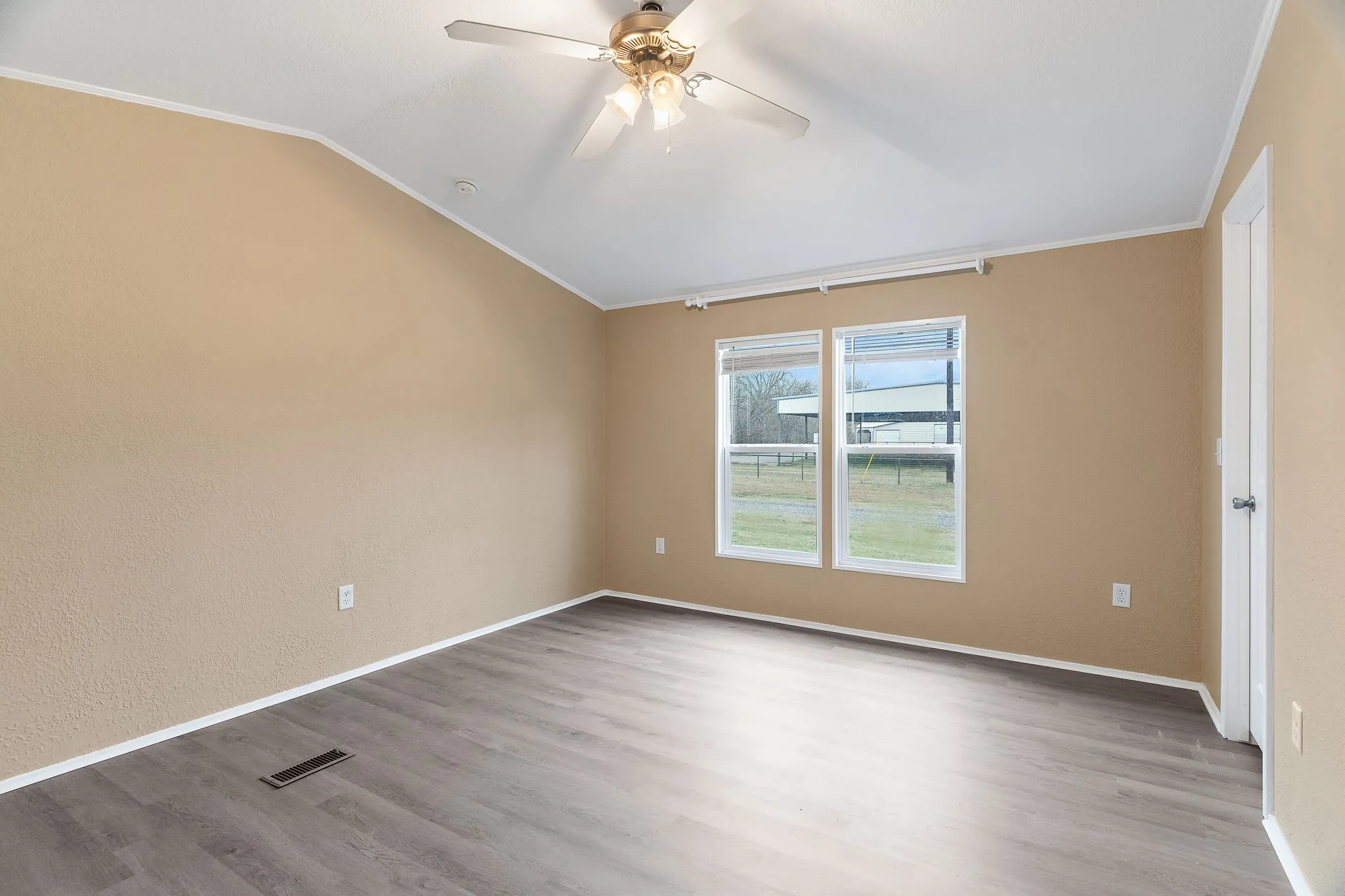 Empty room featuring vaulted ceiling, wood-type flooring, and ornamental molding