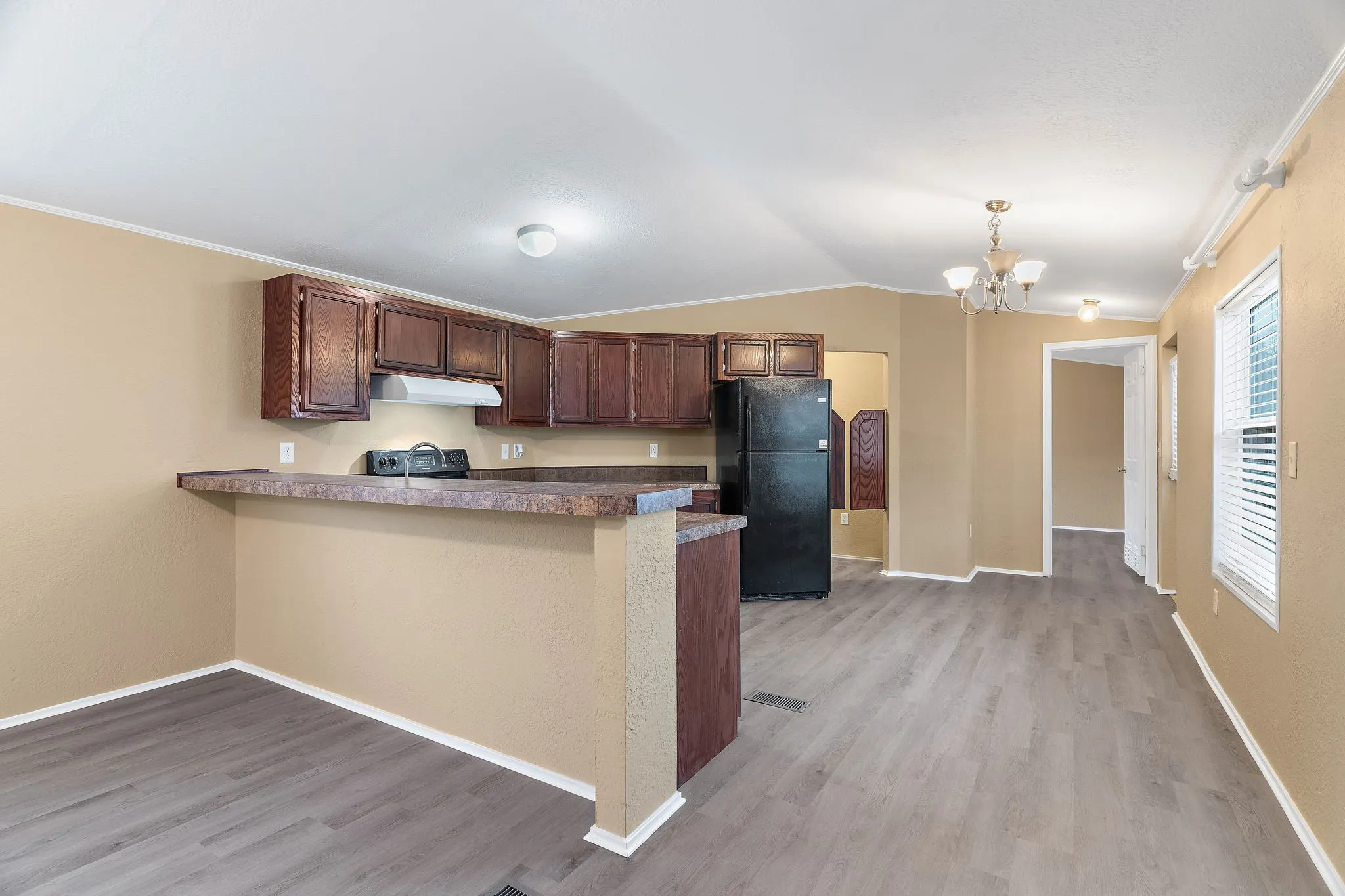 Kitchen with decorative light fixtures, light hardwood / wood-style floors, vaulted ceiling, black fridge, and kitchen peninsula