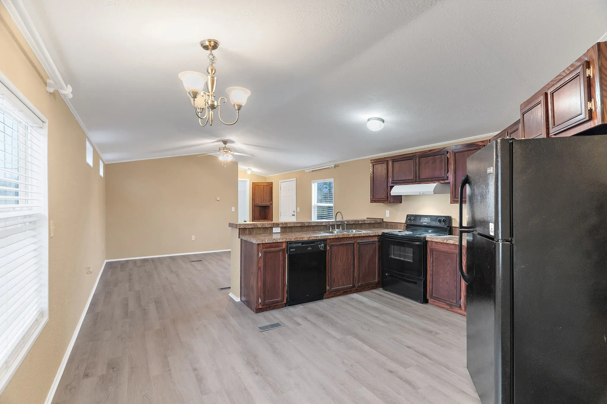 Kitchen featuring kitchen peninsula, light hardwood / wood-style flooring, black appliances, sink, and pendant lighting
