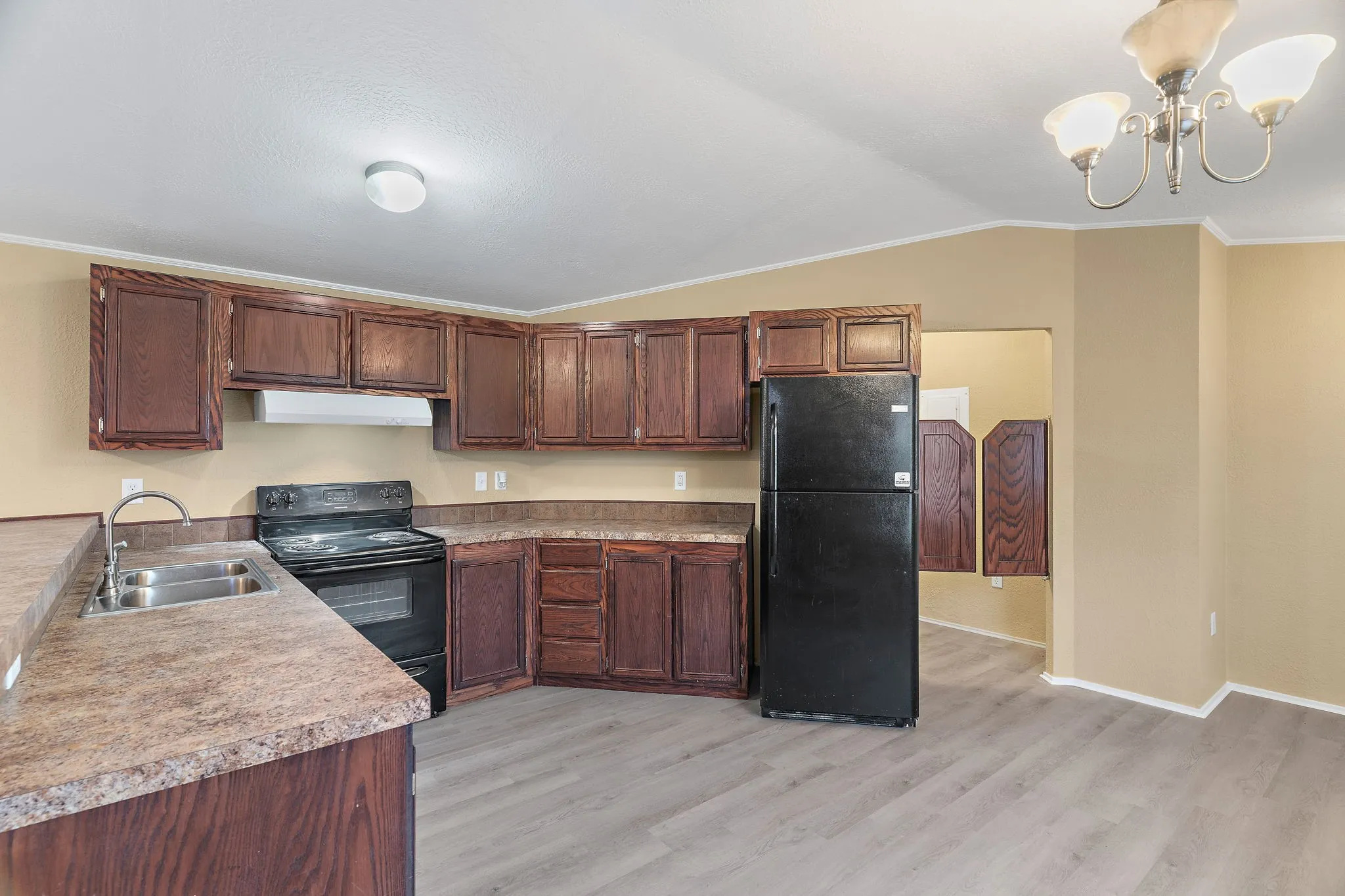 Kitchen with light hardwood / wood-style flooring, black appliances, lofted ceiling, crown molding, and sink