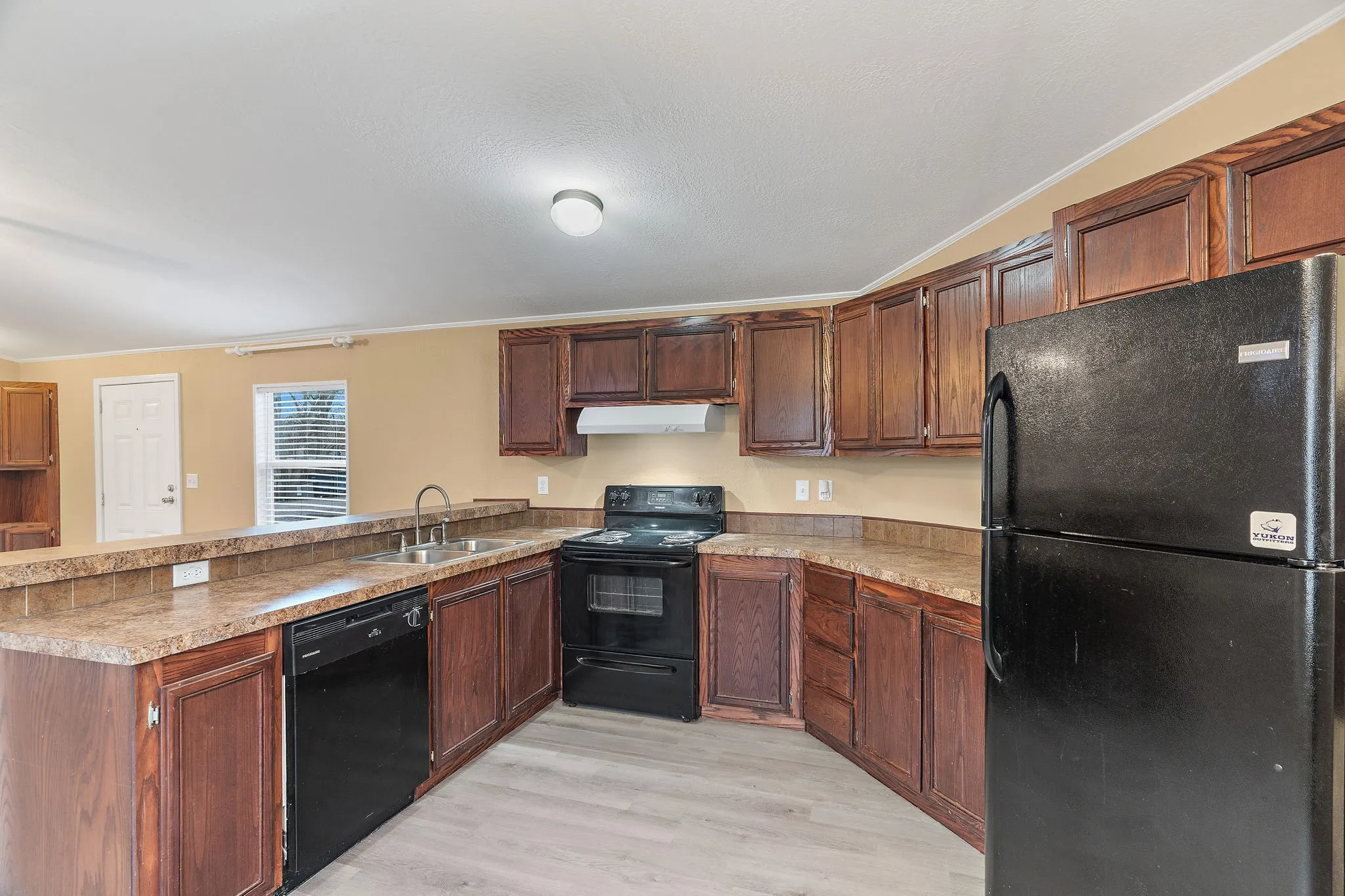 Kitchen with light wood-type flooring, kitchen peninsula, black appliances, sink, and crown molding