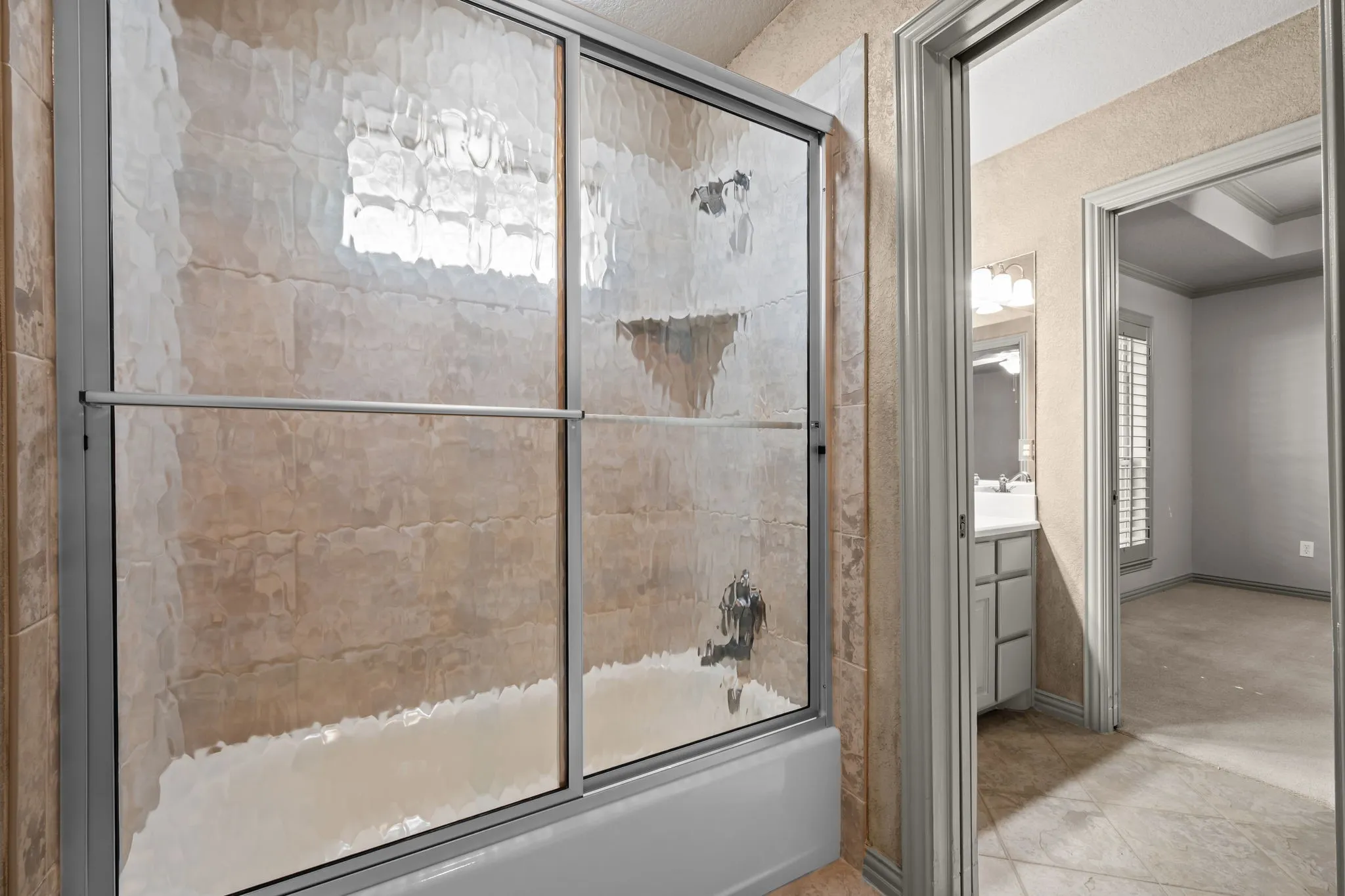 Tub/shower combination featuring a textured tile surround and sliding glass doors