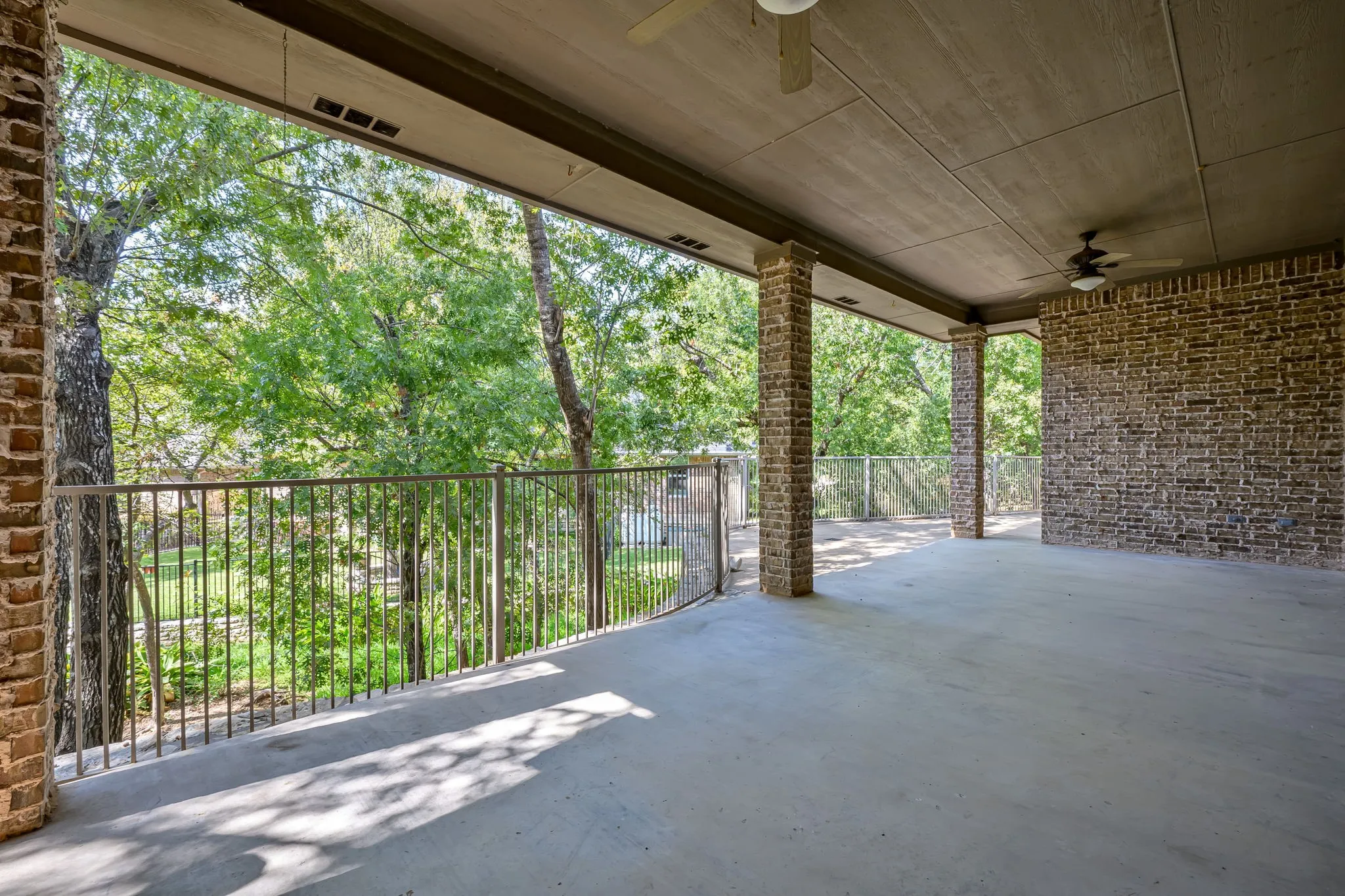 Spacious covered patio featuring concrete flooring, brick columns, and a protective railing overlooking creek