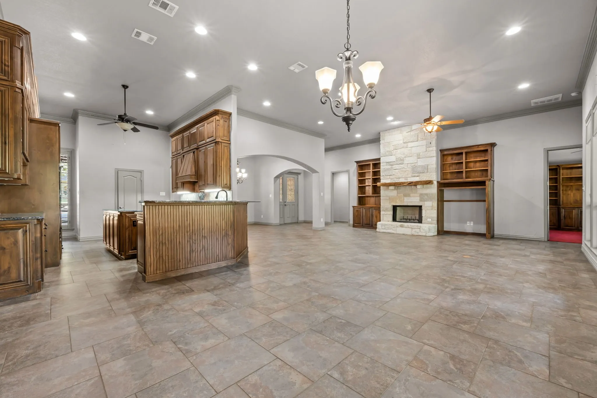 Tile flooring, stone-clad fireplace with wood mantel, recessed lighting, wood cabinetry, and an arched doorway