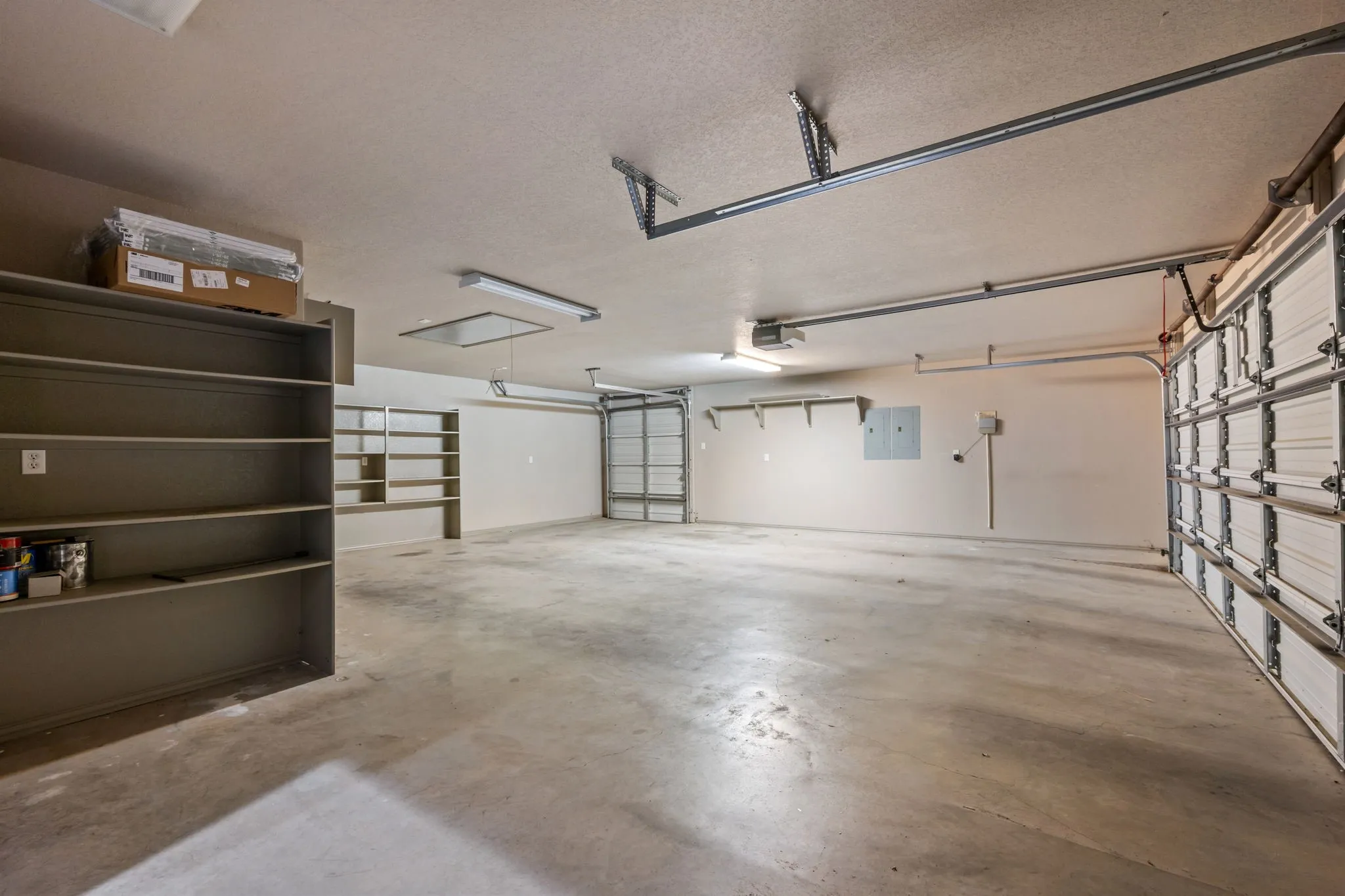 Spacious garage featuring a concrete floor, built-in shelving, two overhead garage doors