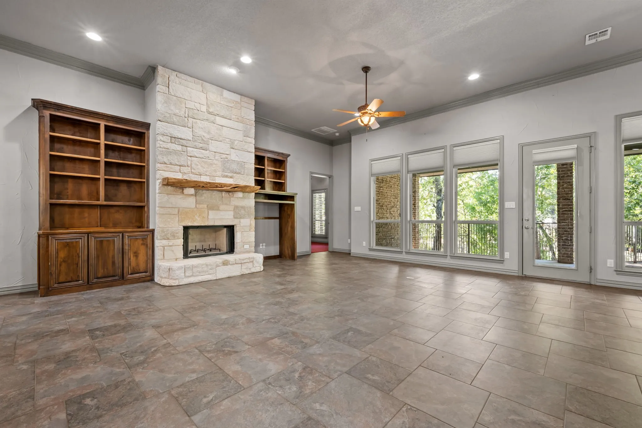Stone-clad fireplace with a wood mantle, built-in shelving, tile flooring, and a ceiling fan