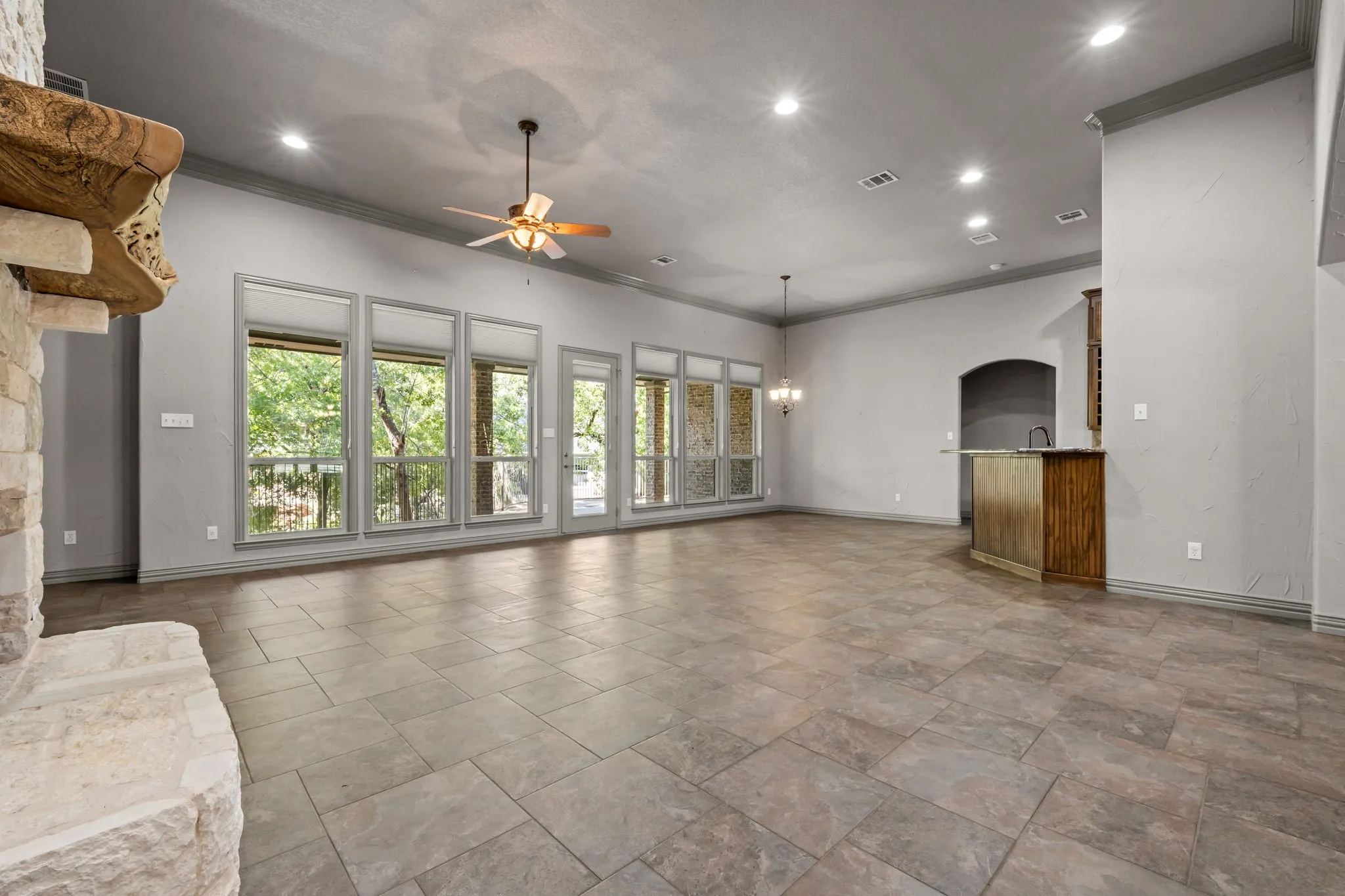 Spacious living area featuring large format tile flooring, a stone fireplace with a carved wood mantel, and multiple windows