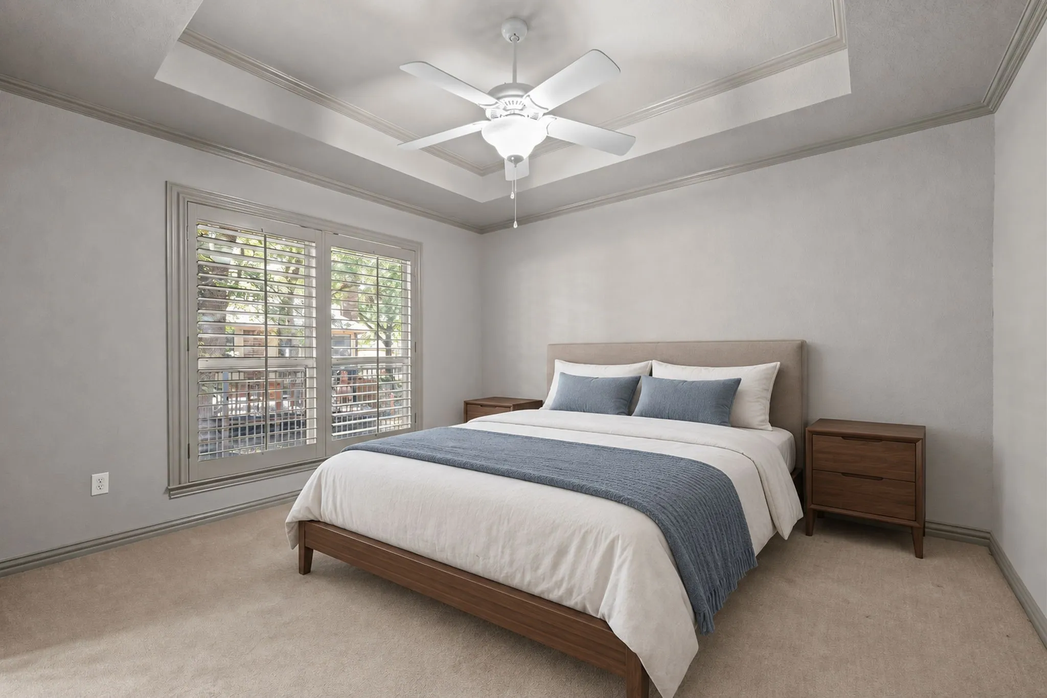Tray ceiling with crown molding, ceiling fan, window with plantation shutters, and carpeted flooring