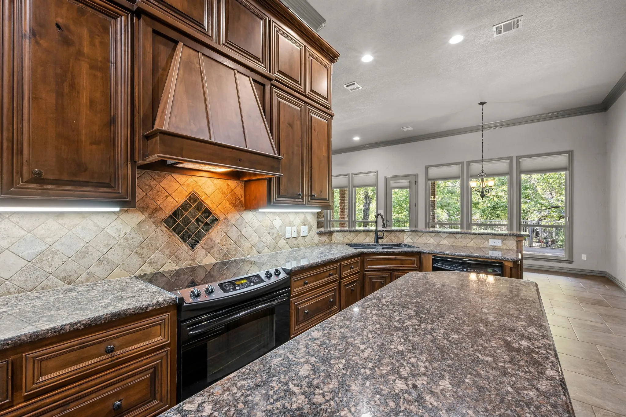 Kitchen featuring wood cabinetry, stone countertops, tile backsplash with decorative inlay, built-in electric range, and a breakfast bar with an undermount sink