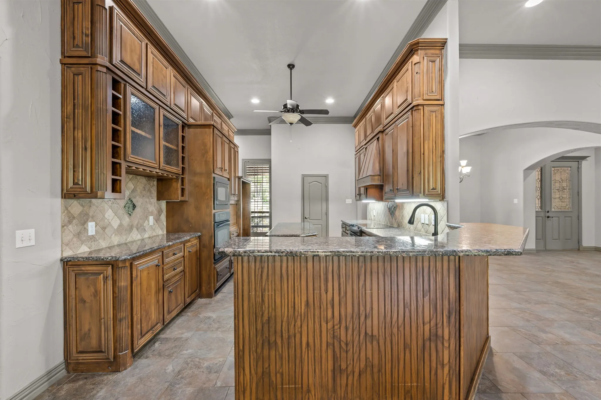 Large kitchen featuring extensive wood cabinetry, stone countertops, a tiled backsplash, and recessed lighting