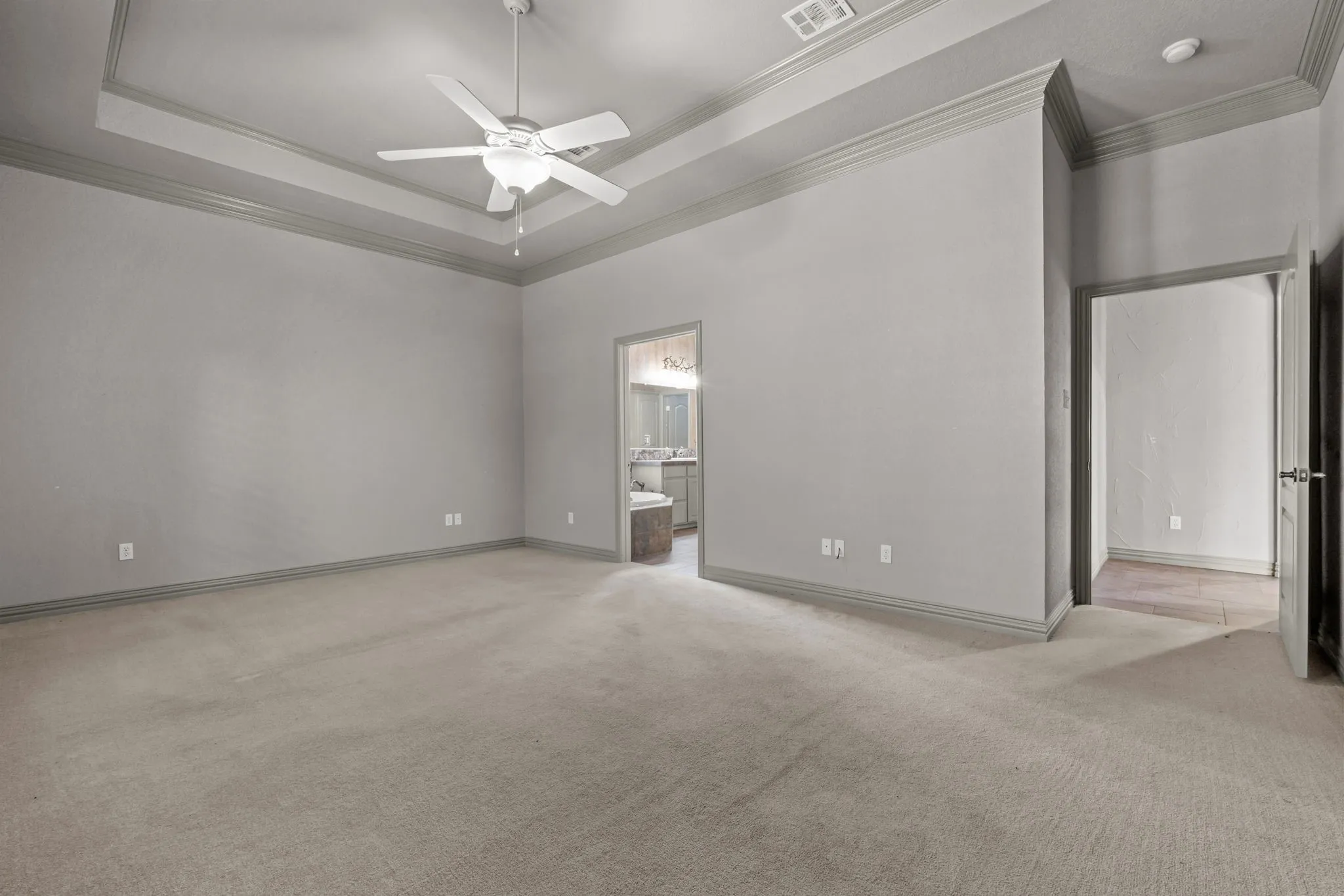 Recessed tray ceiling with crown molding, ceiling fan, and neutral carpet flooring