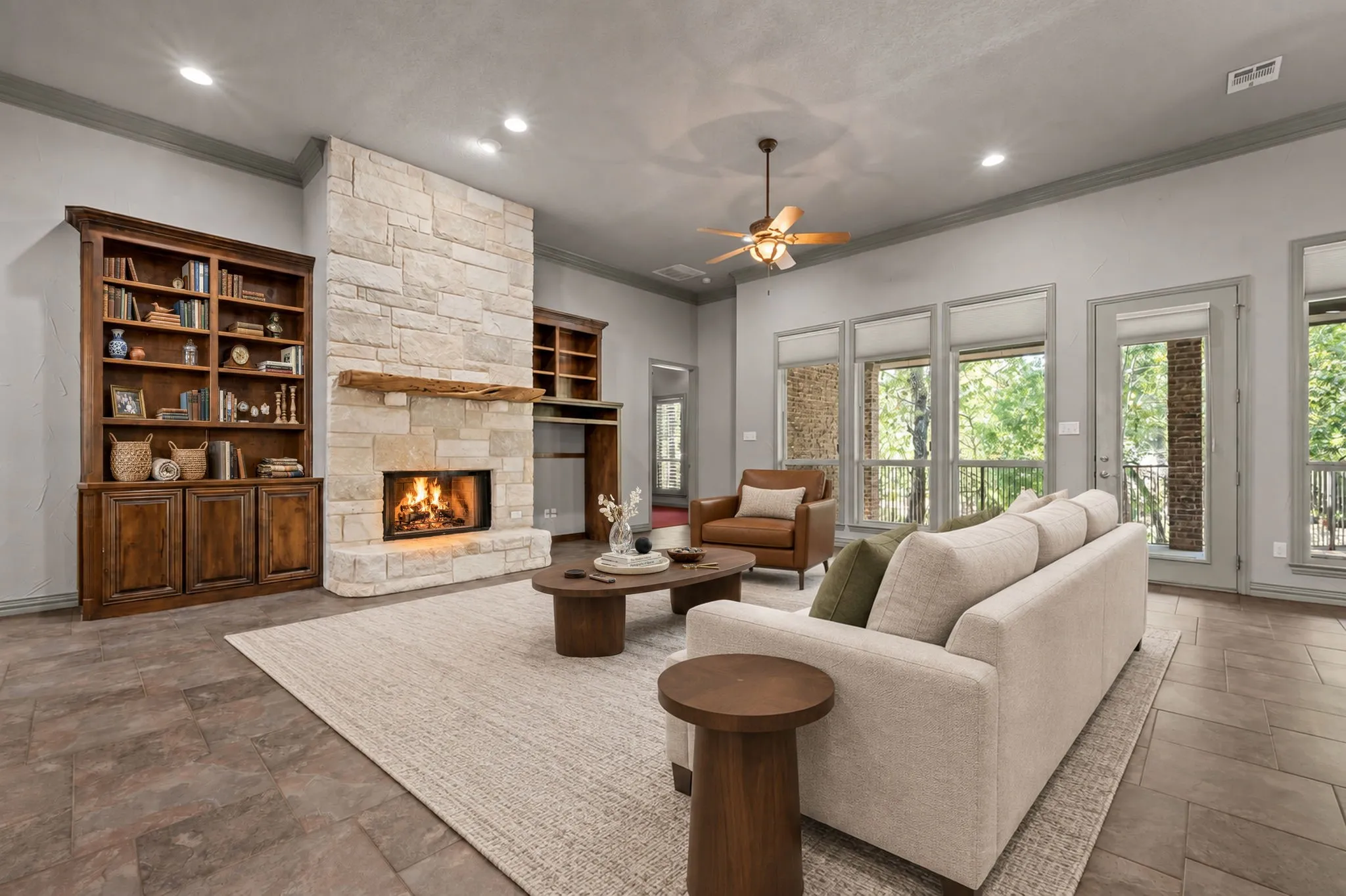 Spacious living room featuring a wood-burning fireplace with stone surround, built-in wood cabinetry and shelving, hardwood flooring, recessed ceiling lighting, and multiple glass doors opening to outdoor spaces. Virtually staged