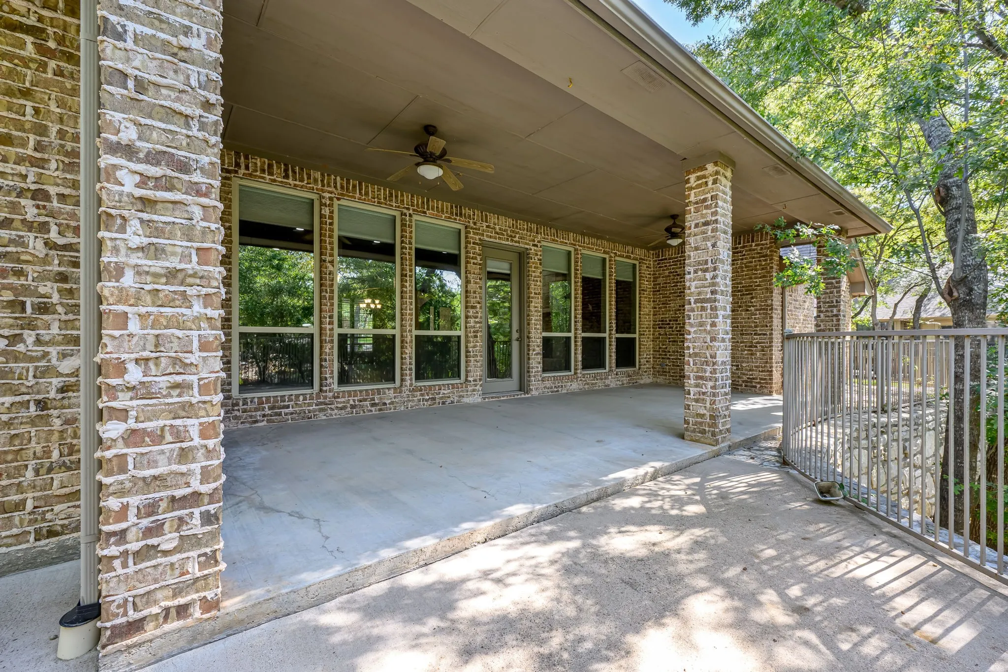 Expansive covered patio featuring brick columns, a ceiling fan, and a metal railing