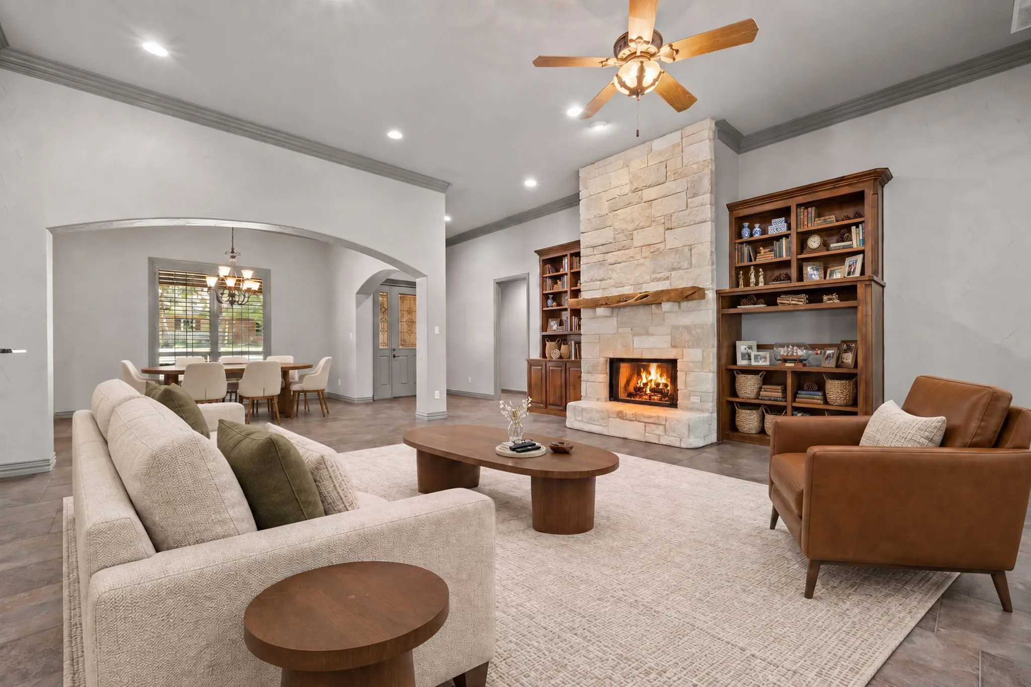 Vaulted ceiling with a wood-finish ceiling fan, stone-clad fireplace with wood mantle, built-in shelving, arched doorways, and tile flooring