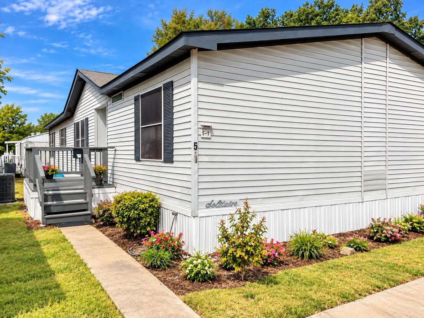 White horizontal siding with dark shutters, front entry with gray steps and handrails, concrete walkway, and landscaped garden beds