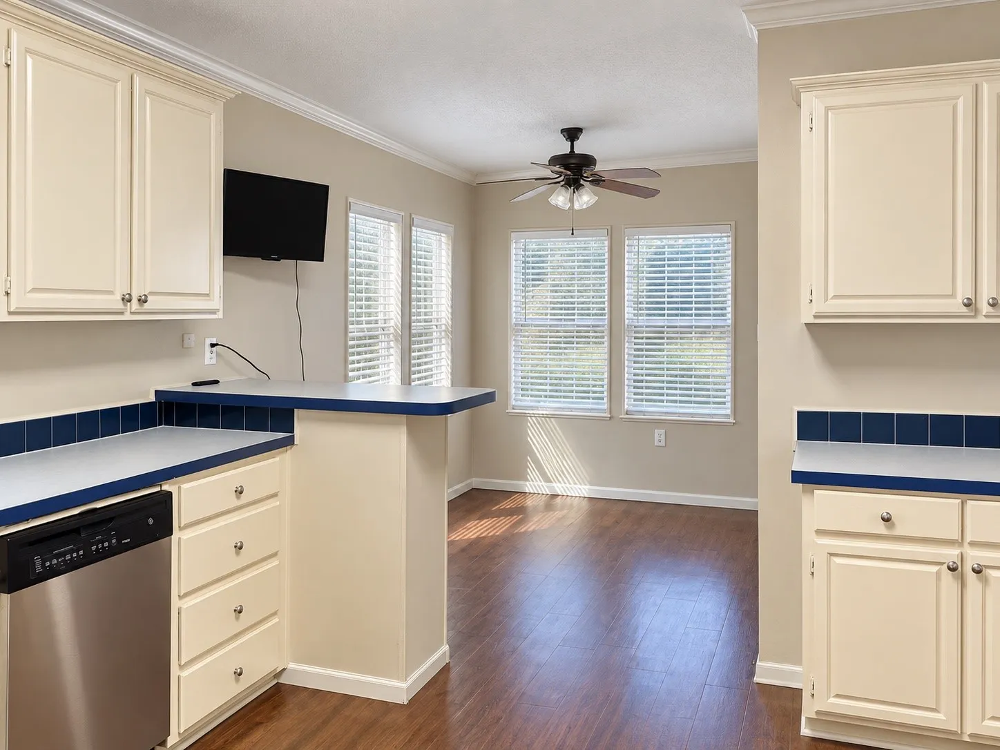 Kitchen featuring cream-painted cabinetry, blue tile backsplash, stainless steel dishwasher, and a breakfast bar