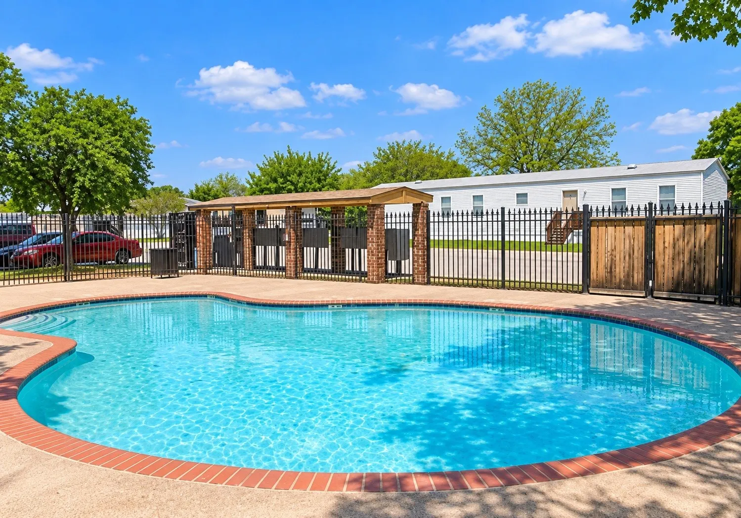 Curved swimming pool with brick coping, concrete decking, and wrought iron fencing with wood gate accents