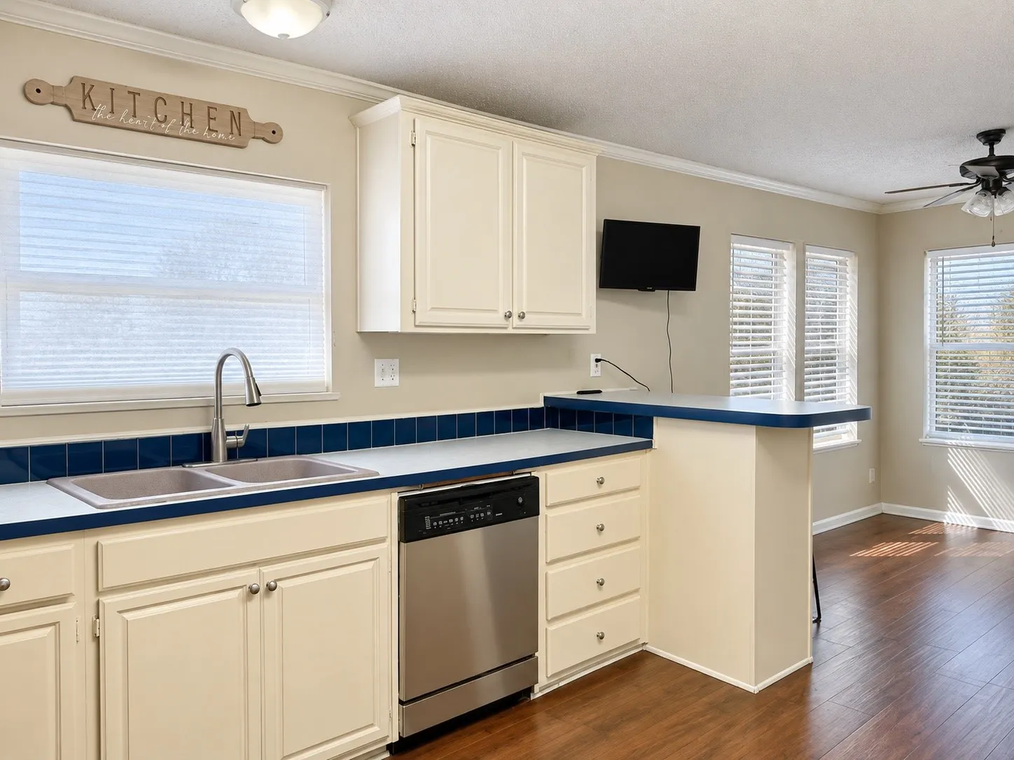 Kitchen featuring cream cabinetry, stainless steel dishwasher, dual basin sink with gooseneck faucet, and breakfast bar