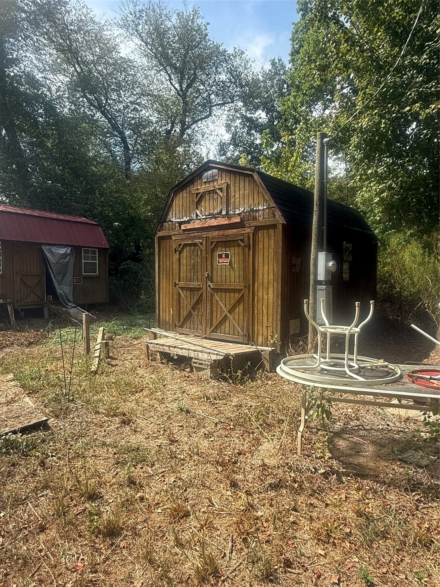 Charming wooden barn-style structure featuring a peaked roof with decorative circular window detail, X-pattern Dutch doors, and metal chimney