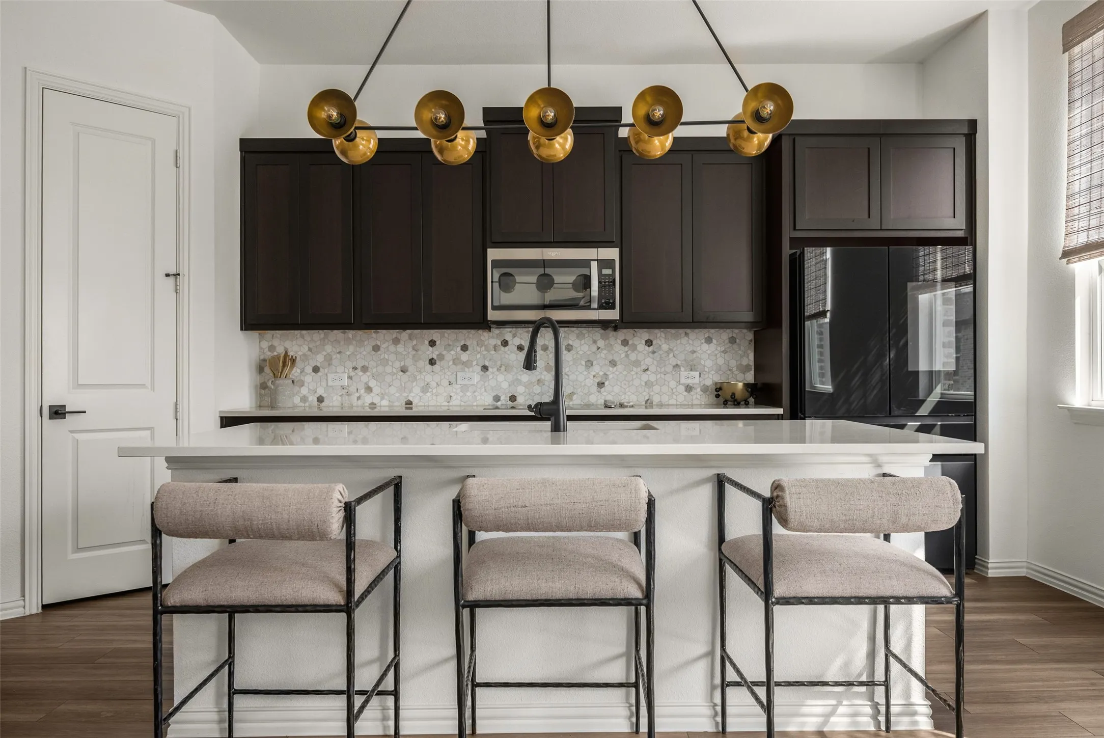 Kitchen featuring dark wood-finish cabinetry, a stone mosaic tile backsplash, built-in microwave, and a black refrigerator
