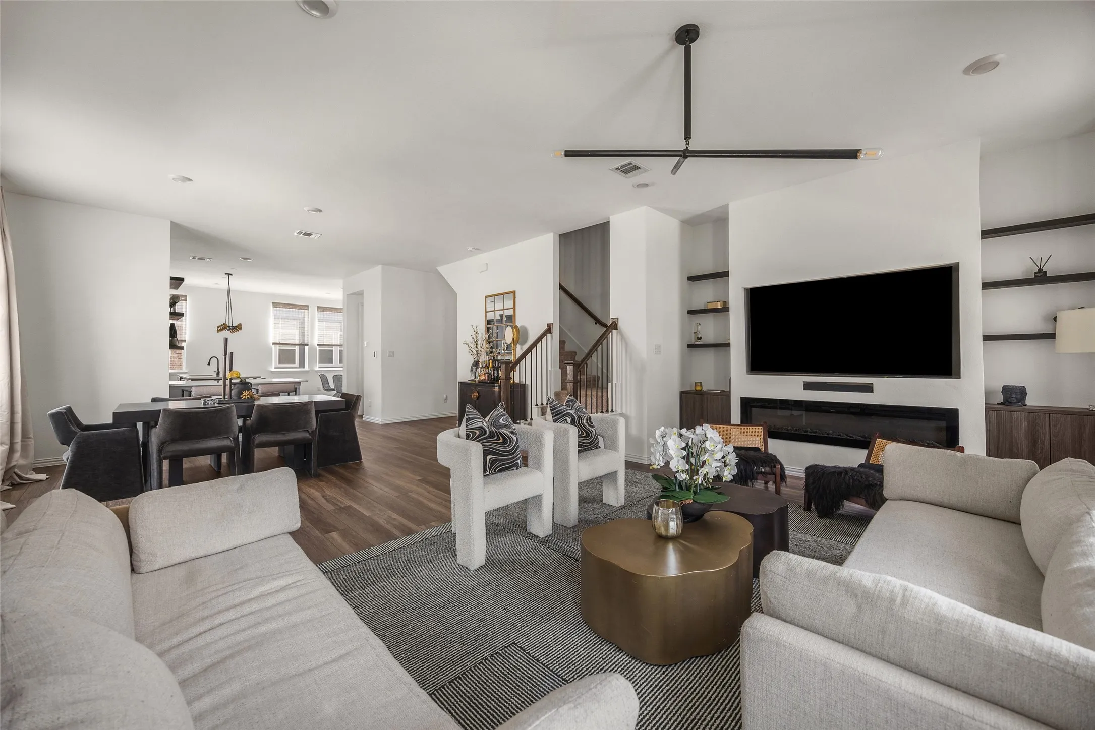 Open-concept living space featuring wood-finish flooring, built-in shelving, an integrated linear fireplace, and a contemporary ceiling fixture